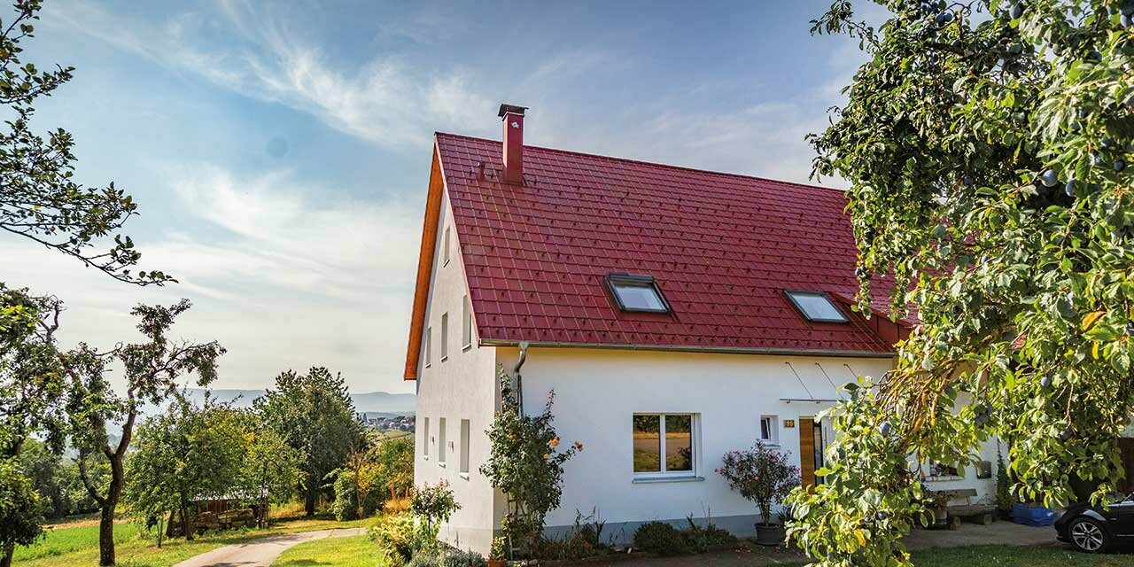 Romantic rural cottage surrounded by trees and shrubs. Covered with a PREFA roof in oxide red.