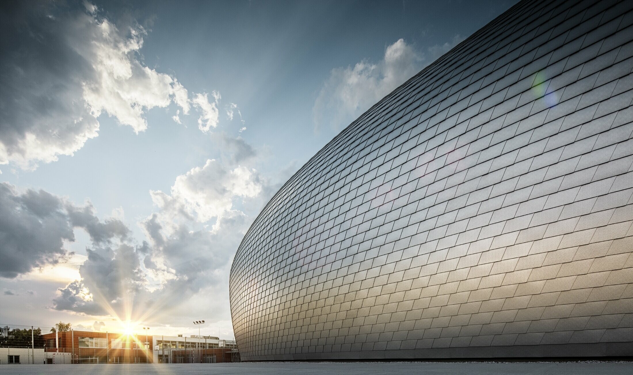 Sports hall in the Czech Republic in the shape of a UFO clad in the PREFA façade shingle in plain aluminium at dawn.
