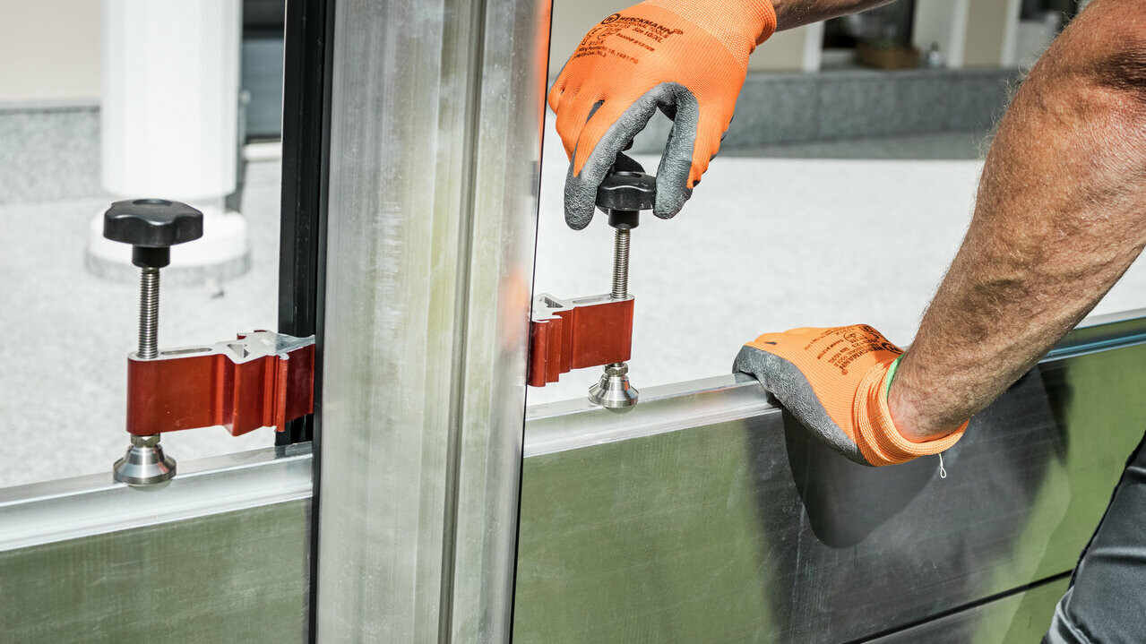 You can see the hands of a gentleman using the compression clamp to fasten the barrier panel of the PREFA flood protection wall.