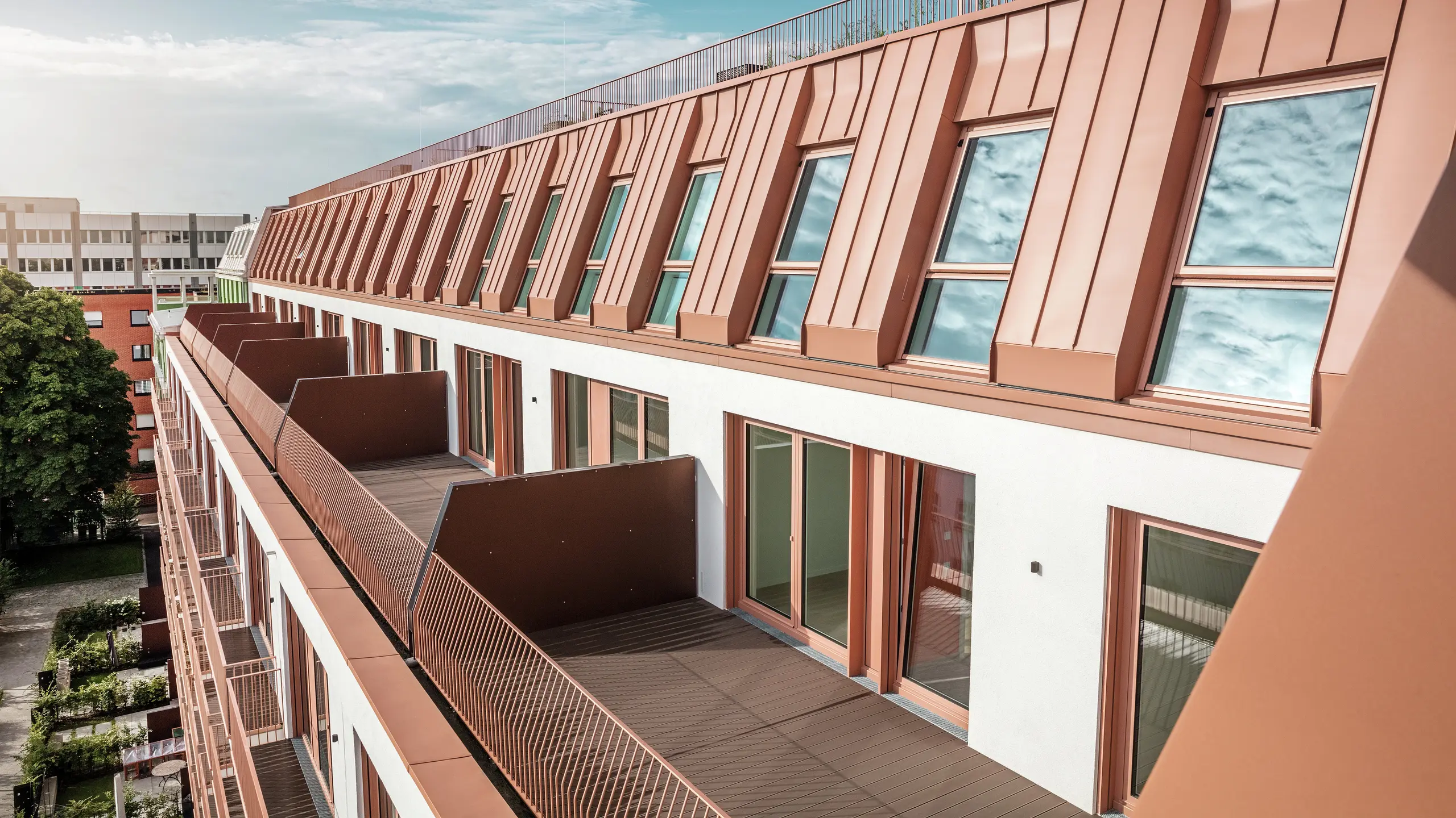 Detailed view of the modern roof and façade design of the Van B residential project in Munich with the high-quality PREFALZ aluminium roof in IGP Orange HDP from PREFA. The precise workmanship of the durable and low-maintenance material offers optimum protection against the elements and gives the building a uniform, elegant appearance. The generous windows and balconies provide plenty of daylight and create an open, liveable living environment with architectural appeal.