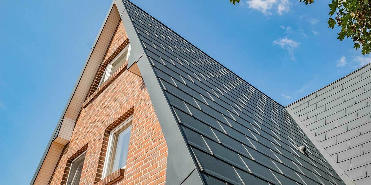 Gabled roof of an A-frame house covered with the PREFA roof tile in anthracite and a brick façade.