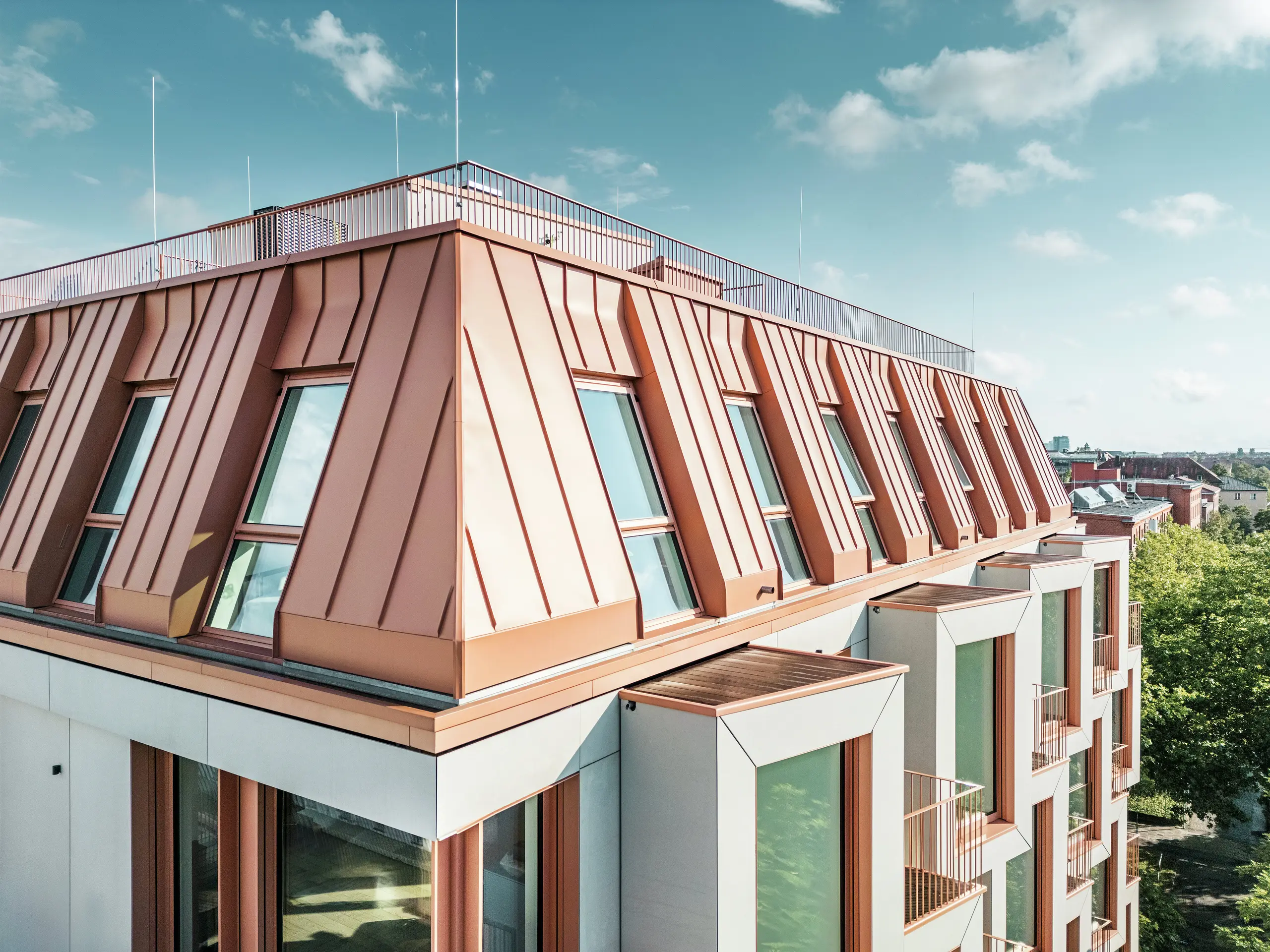 Detailed view of the striking PREFALZ roof covering on the Van B residential building in Munich. The colour-coordinated aluminium roof impresses with its high-quality workmanship, extreme durability and weather resistance. The sloping windows and clearly structured façade elements round off the innovative design concept. Ideal for modern architecture, where functionality and aesthetics go hand in hand in urban residential construction. The row of bay windows can be seen at the bottom of the picture.