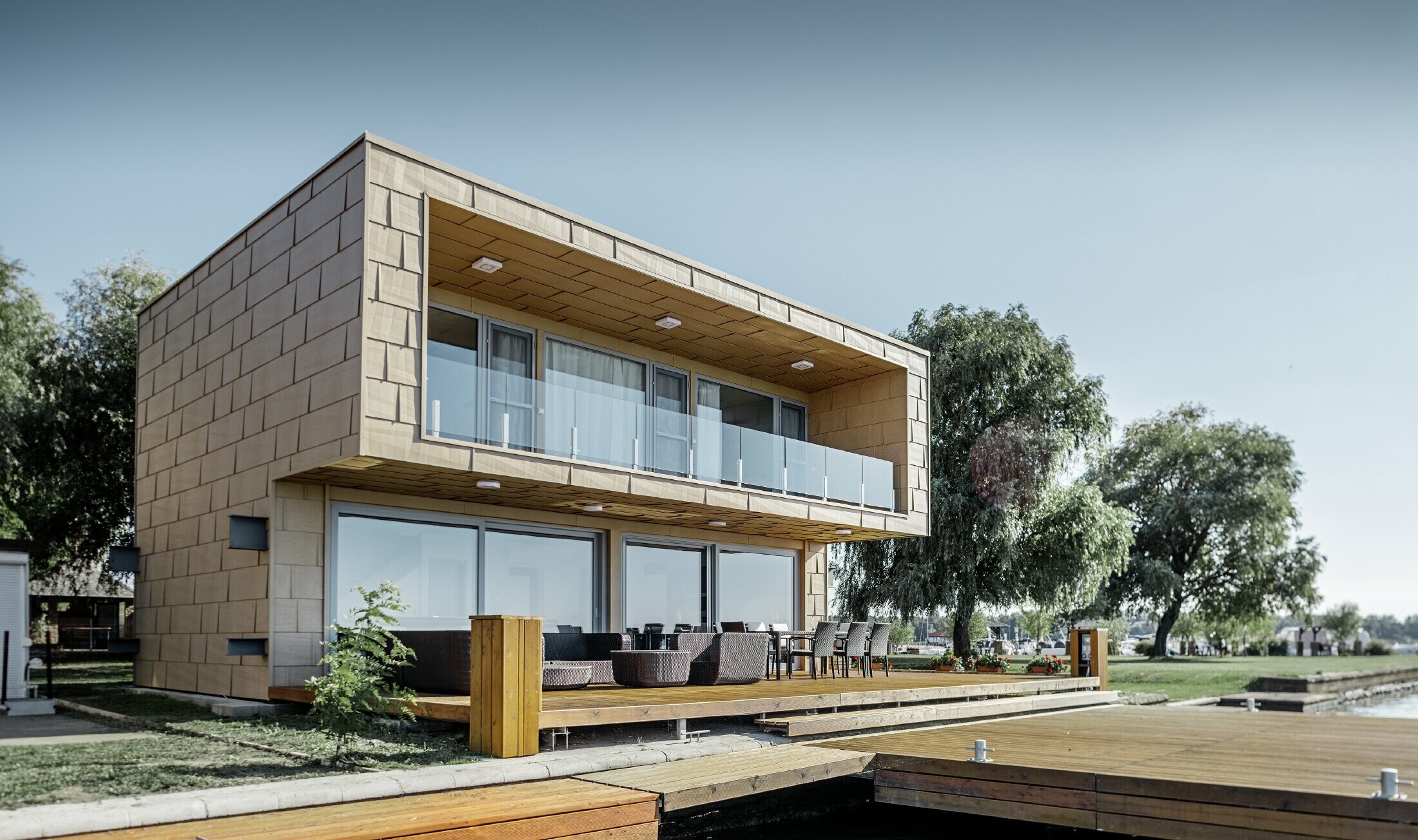 Modern lakeside weekend residence with a flat roof, large windows and a canted aluminium façade in sand brown