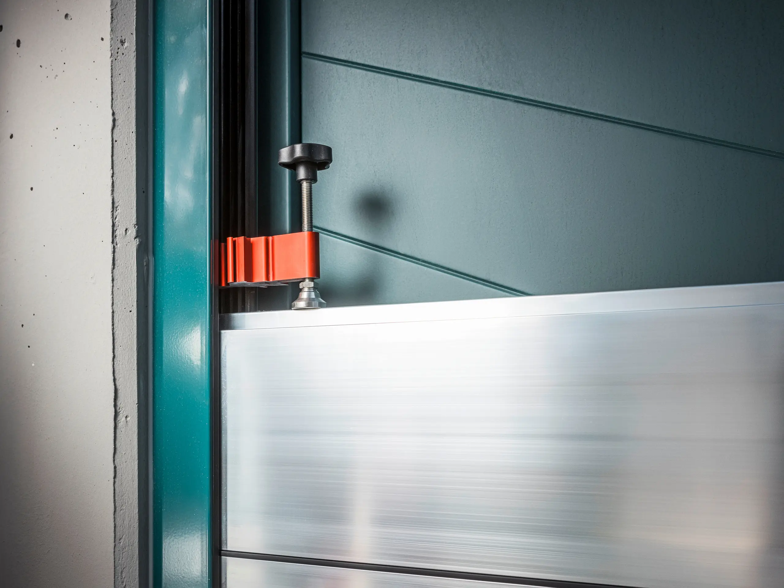 Detailed view of the PREFA flood protection system on a gate frame, consisting of aluminium barrier panels that are fastened with a robust, red clamp (the compression clamp) to ensure reliable protection against flooding.
