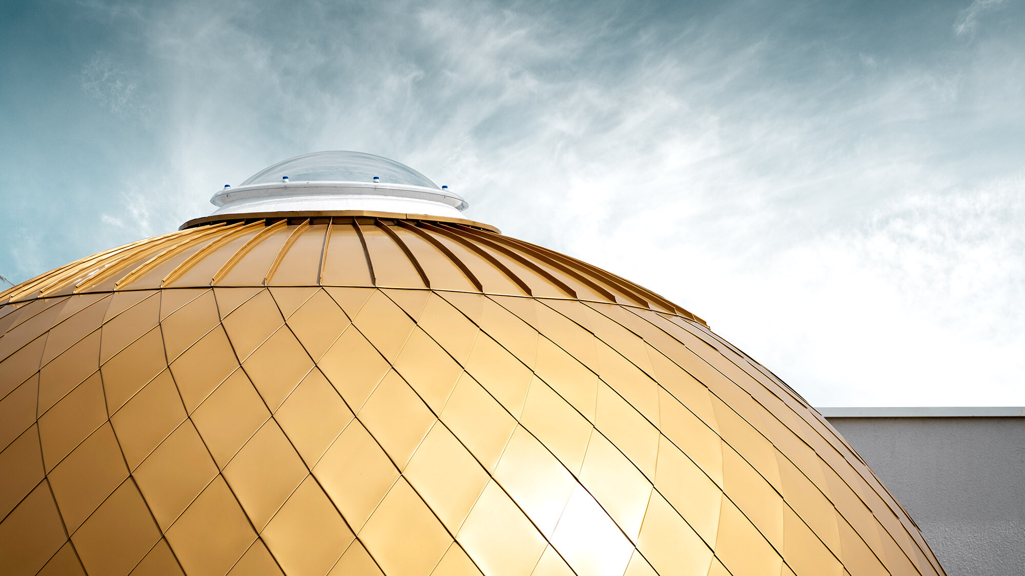 Detail view of one of the spheres with a central skylight, the sky above it is lightly streaked with clouds.