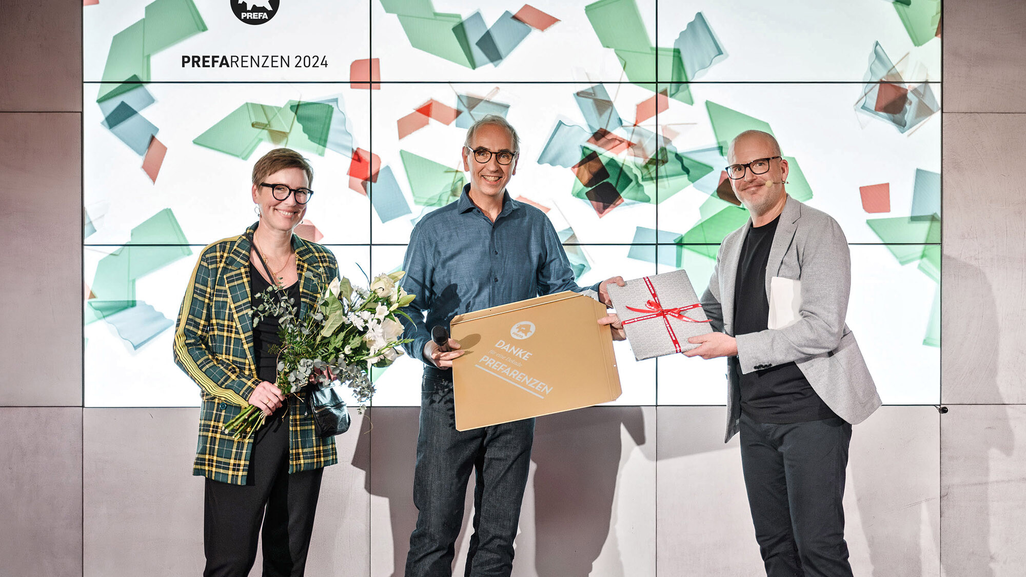 The photographers Juliane Croce and Wolfgang Croce with International Marketing Manager Jürgen Jungmair, who is handing them a gift in front of the presentation area.