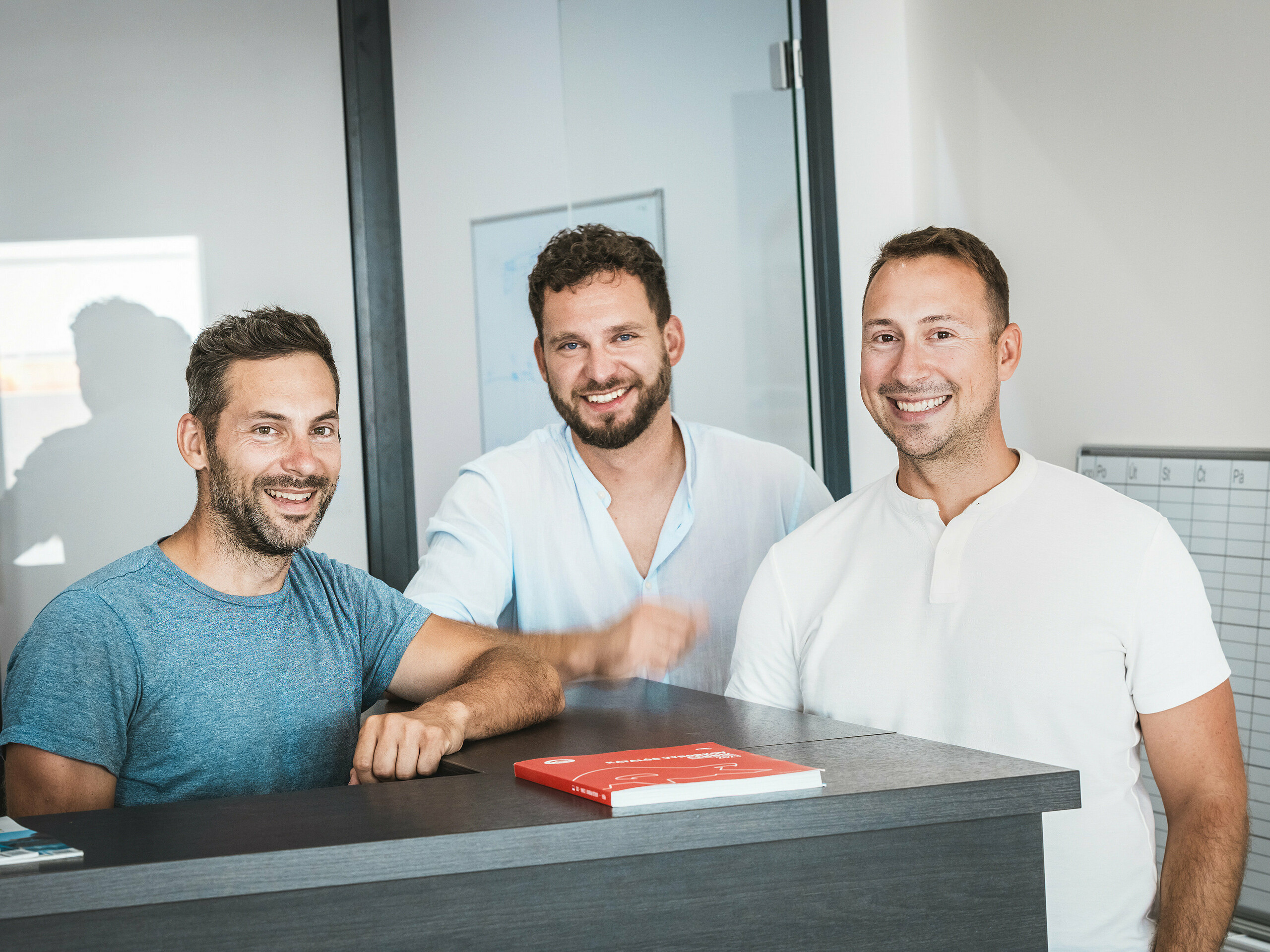 An einem Empfangstresen in einem modernen Büro stehen die Brüder Juraj und Peter Pekár sowie Tomáš Filo von der Spengler-Firma Prvá Strechárska und geben einen authentischen Einblick in das Projektteam hinter dem Stadtquartier Vydrica in Bratislava. Als zentrale Akteure realisierten sie die komplexen Dachlandschaften mit PREFA-Aluminium-Dachschindeln, die durch Präzision, Langlebigkeit und Witterungsbeständigkeit überzeugen und maßgeblich zur hochwertigen, nachhaltigen Gebäudehülle des Quartiers beitragen.