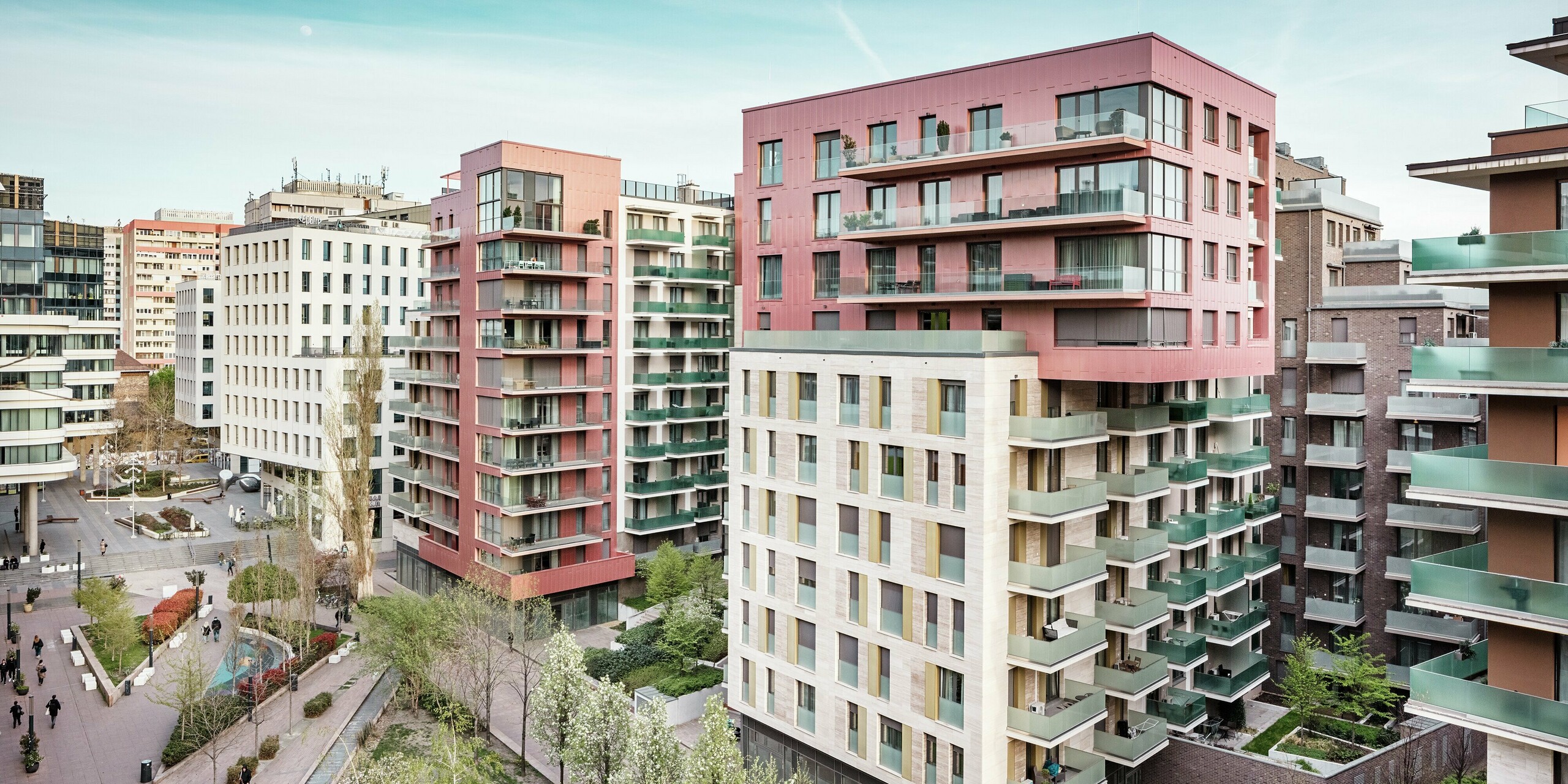 Stimmungsvolle Gesamtansicht des Grand Corvin Ensembles im Budapester Corvin-Viertel. Die markanten Obergeschosse sind mit PREFA Siding Fassadenpaneelen in vertikaler Verlegung und Sonderfarbe Lachsmetallic gestaltet. In Kombination mit Naturstein und großzügigen Glasflächen entsteht ein modernes, hochwertiges Stadtbild. Die langlebige Aluminiumfassade betont die architektonische Vielfalt und den nachhaltigen Anspruch der umfassenden Stadterneuerung.