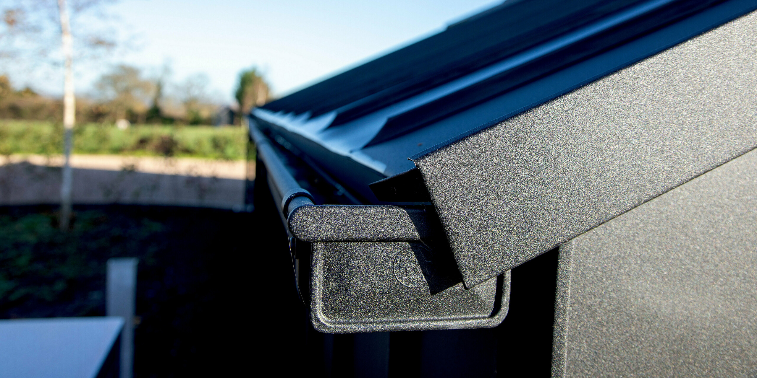 Close-up view of a modern PREFA roof design featuring PREFALZ in P.10 black. The precisely crafted aluminum box gutter and clean roof edges create striking architectural lines. The durable, weather‑resistant aluminum surface delivers long‑lasting protection while enhancing the building’s contemporary aesthetic in an outdoor setting.