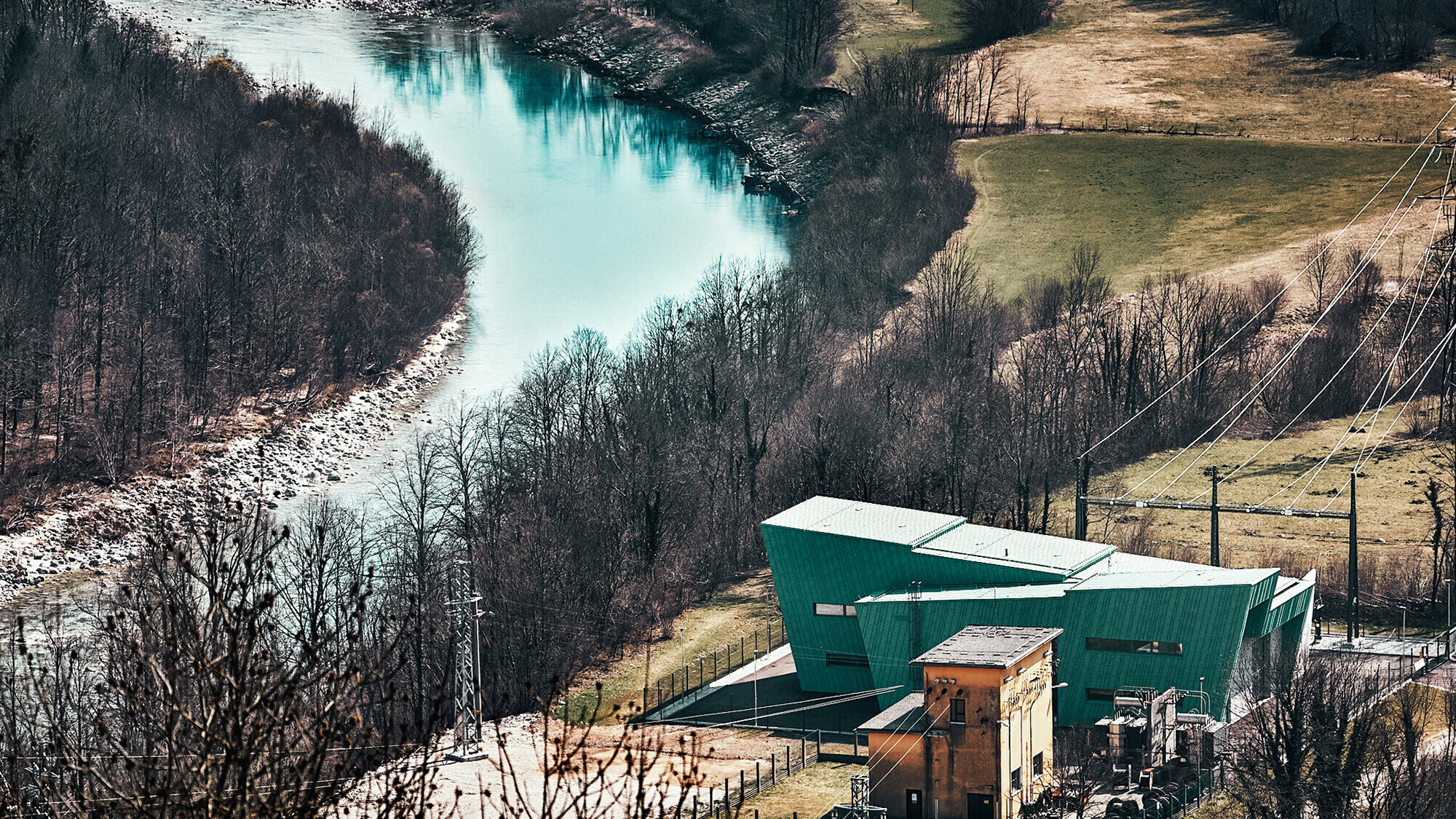 The substation from a bird eye's perspective, the roof surfaces running past each other are particularly visible, the old substation stands right next to it. The colour of the façade is the same as that of the Soča river running past it.