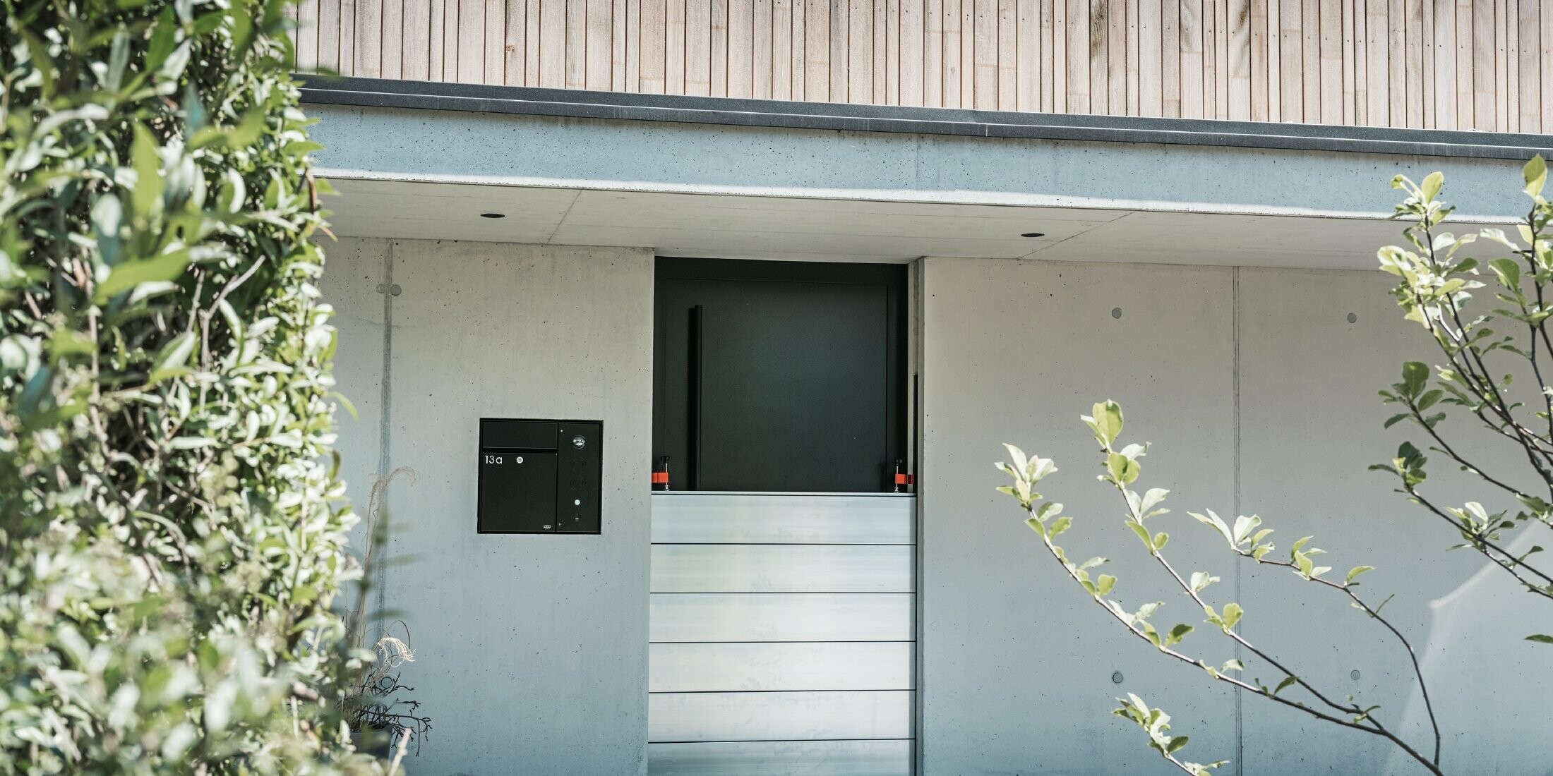 PREFA flood protection is installed in front of the entrance door of a detached house with a wooden façade. 