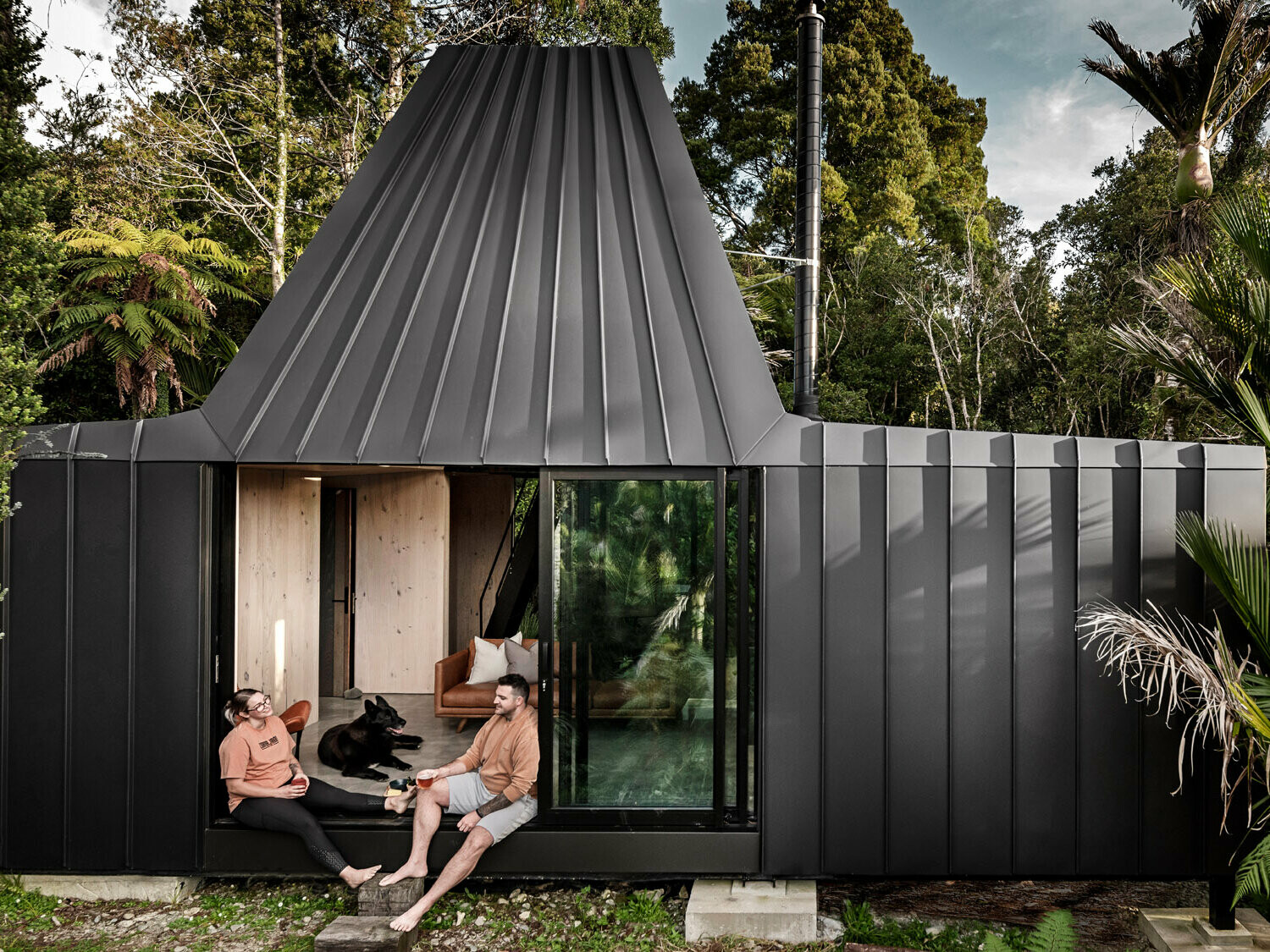 Overall view of the bivouac, the sliding door is open and two people and a dog are sitting in the transition area. The complex roof geometry is in view.