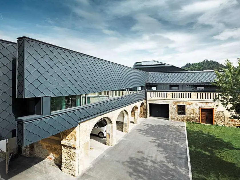 The BH Völkermarkt building is a mixture of old and new building materials, the ground floor is still made from old stone wall, while the upper floor is clad with modern PREFA roof tiles 29 × 29 in anthracite.