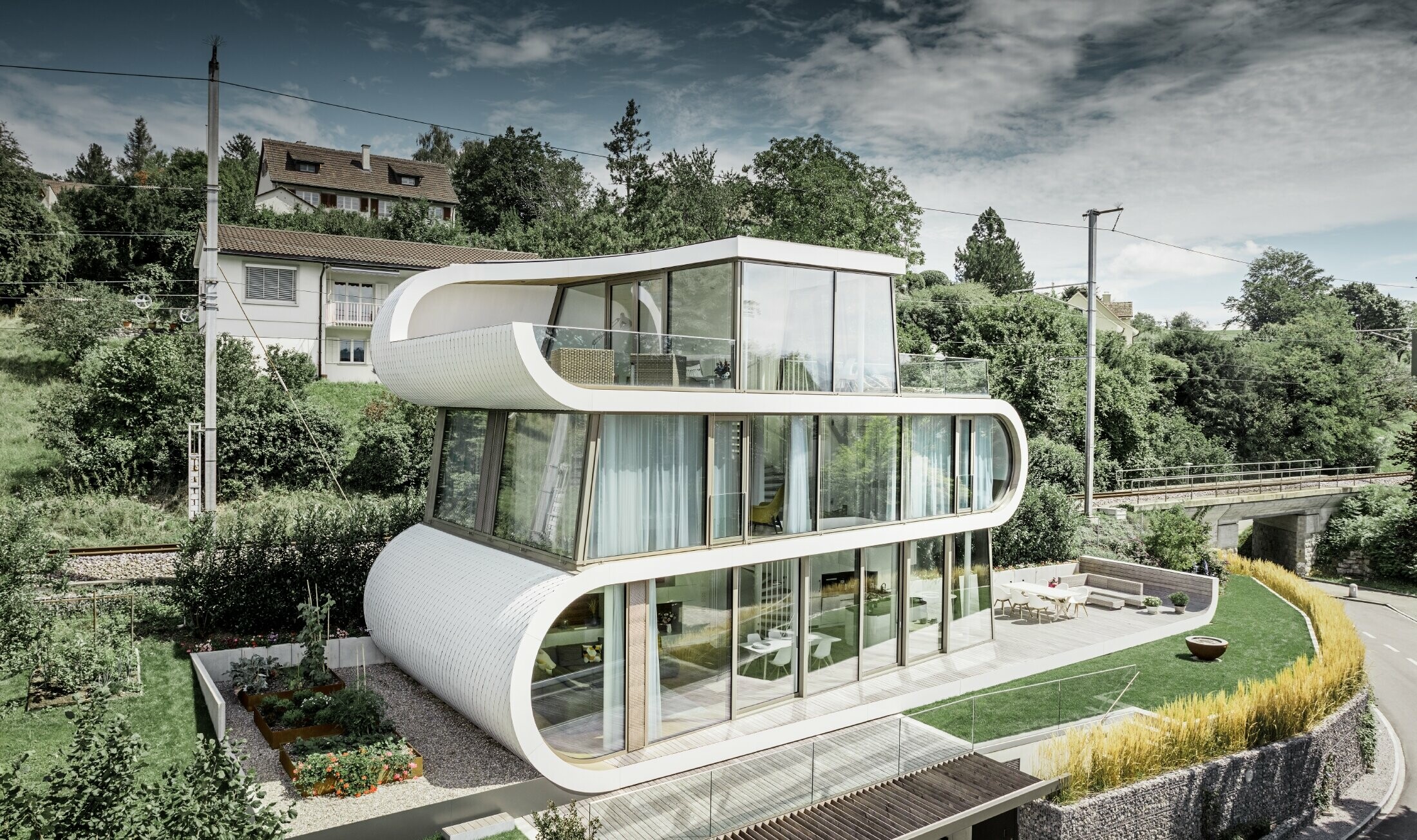 Ultra modern detached house designed by the architect Camenzind from Zurich. A curved truss connects the individual levels. The curves were clad in the PREFA small rhomboid roof tile in pure white. The house has numerous large glazed areas creating a very open effect.