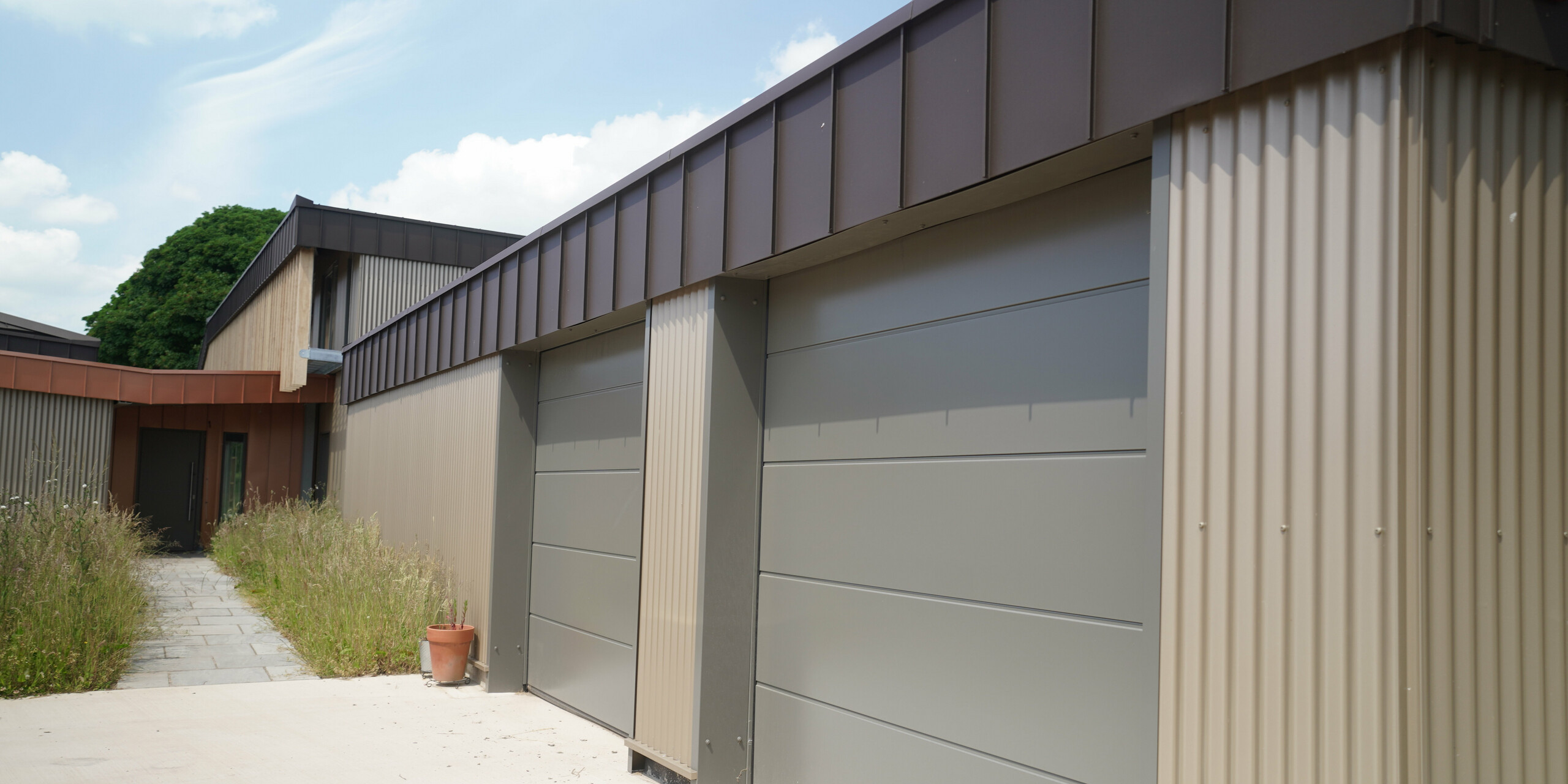 Garage doors of a longhouse in Derbyshire - the building is wrapped in PREFALZ in P.10 Brown and wooden elements