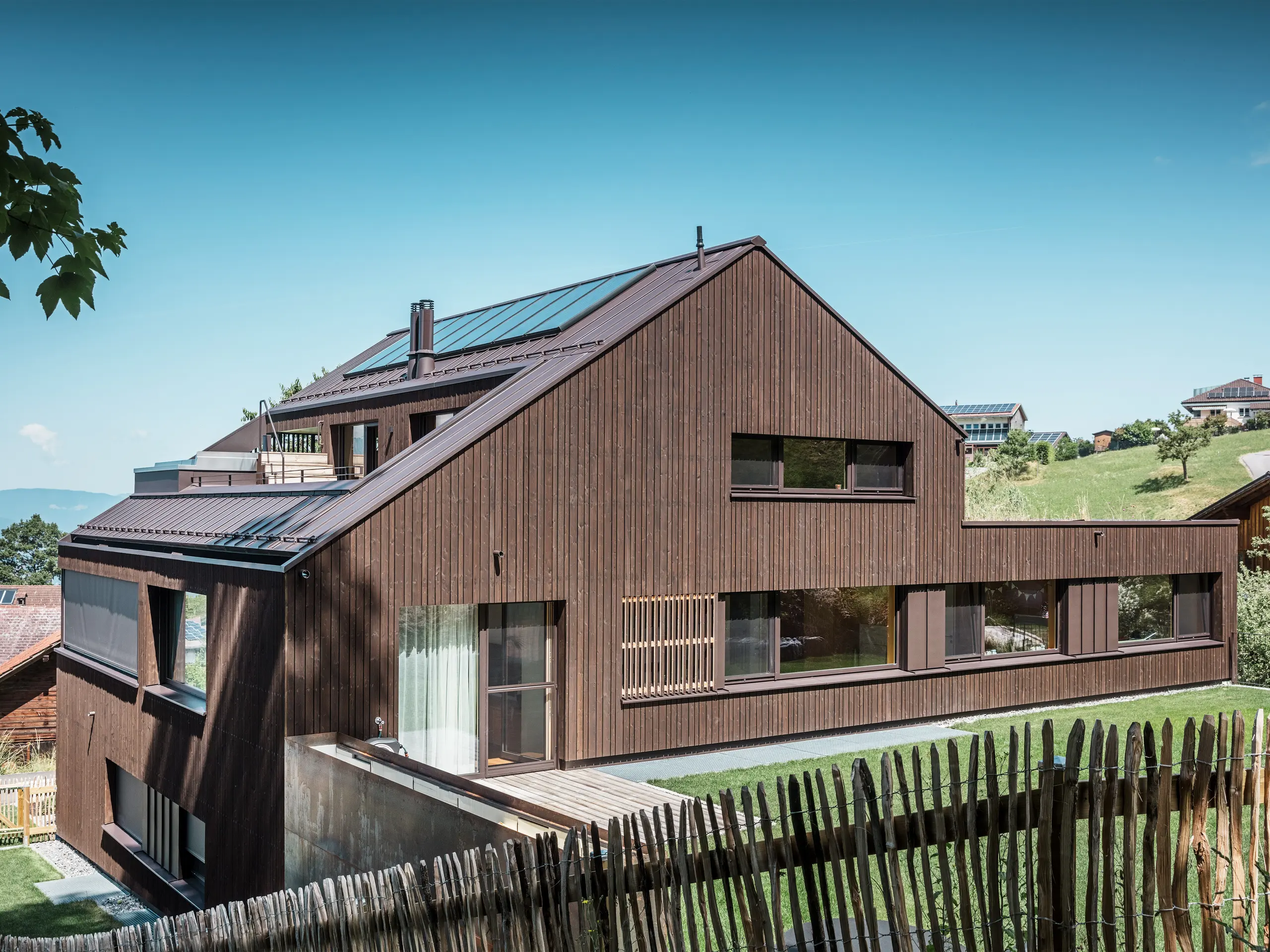  The monochrome multi-family house with the aluminium roof and the silver fir façade from a lateral perspective after the conversion.