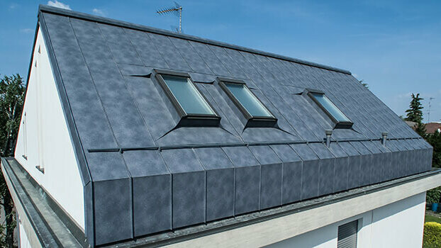 Loft conversion of a gable roof with roof-top windows. The roof goes directly into the façade and was clad with standing seam roofing in stone grey Prefalz.