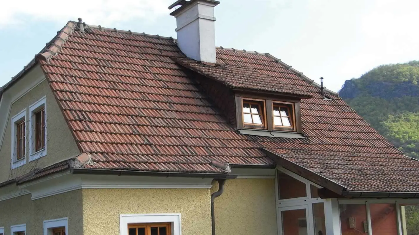Old detached house with a tiled roof and a rough, yellow rendered façade before roof renovation