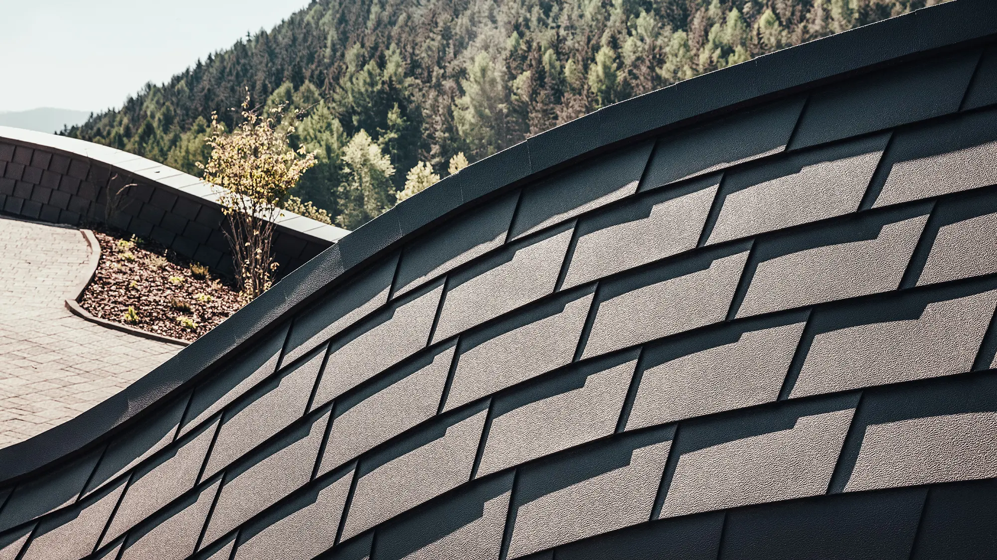 Detailed view of PREFA façade shingles in P.10 Brown. A section of the forest can be seen in the background