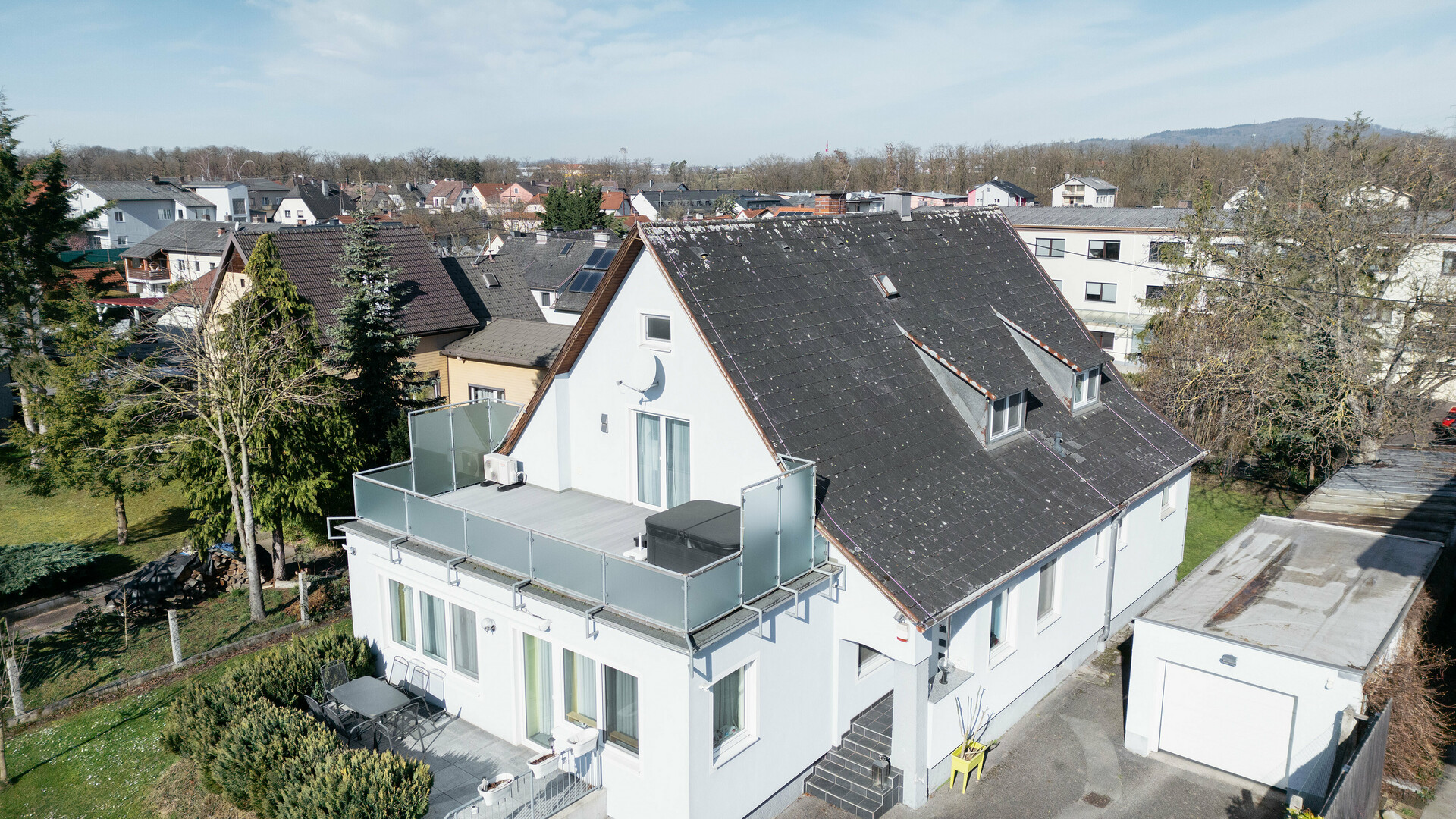 A bird's-eye view of a building with an old Eternit roof covered in dirt and lichen. No solar panels are visible on the roof. The balcony in the foreground has a glass railing and is located on the top floor of the building.