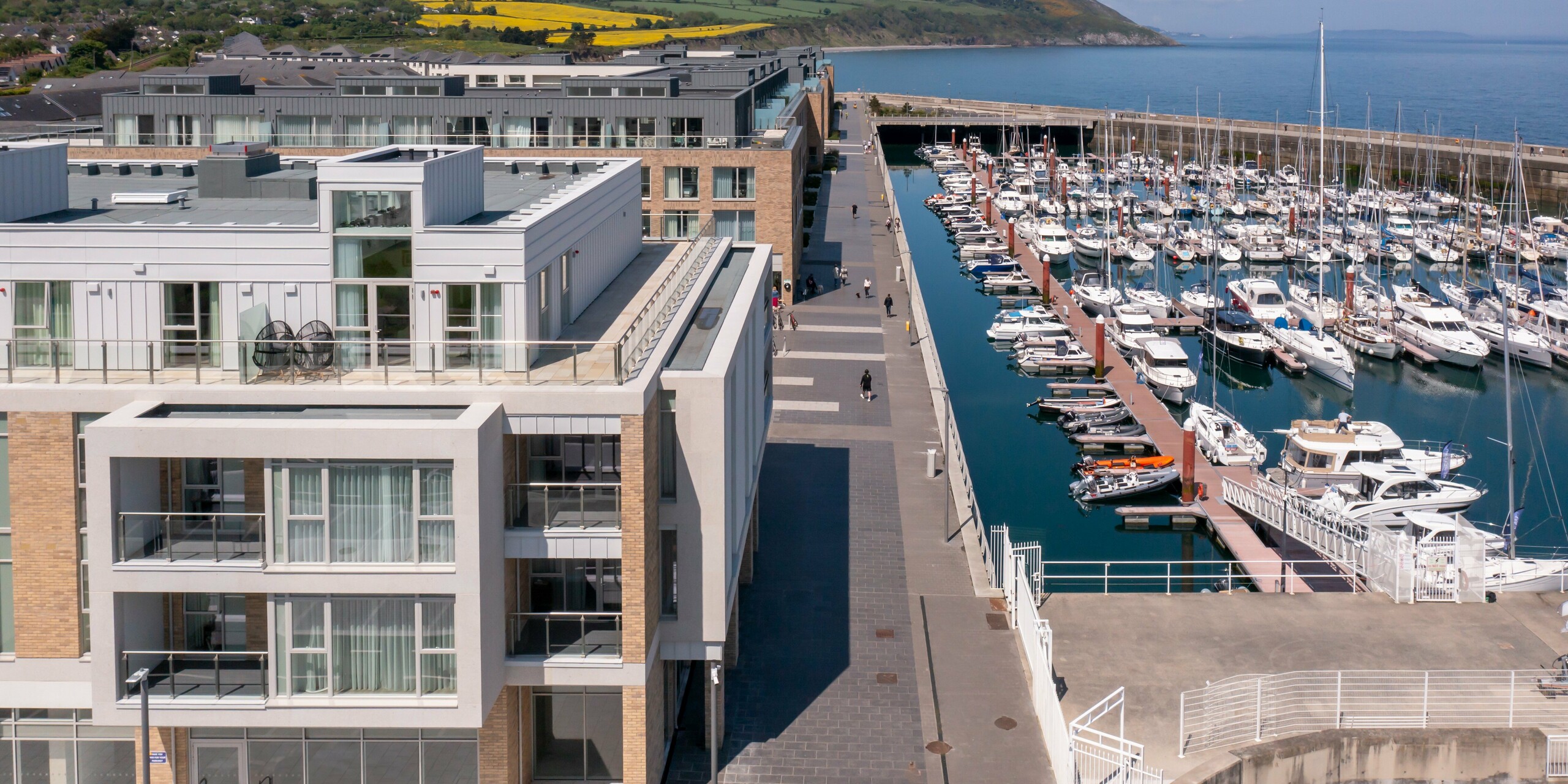 Aerial view of Marina Village Greystones in Wicklow, Ireland - a modern residential development located directly on the marina. Approximately 2,000 m² of PREFALZ in P.10 Prefa White and P.10 Light Grey are used for the façade of the residential complex. Elegant architecture with generous glass fronts and balconies, surrounded by a picturesque landscape on the water. The high-quality aluminium cladding from PREFA offers durable protection and timeless aesthetics.