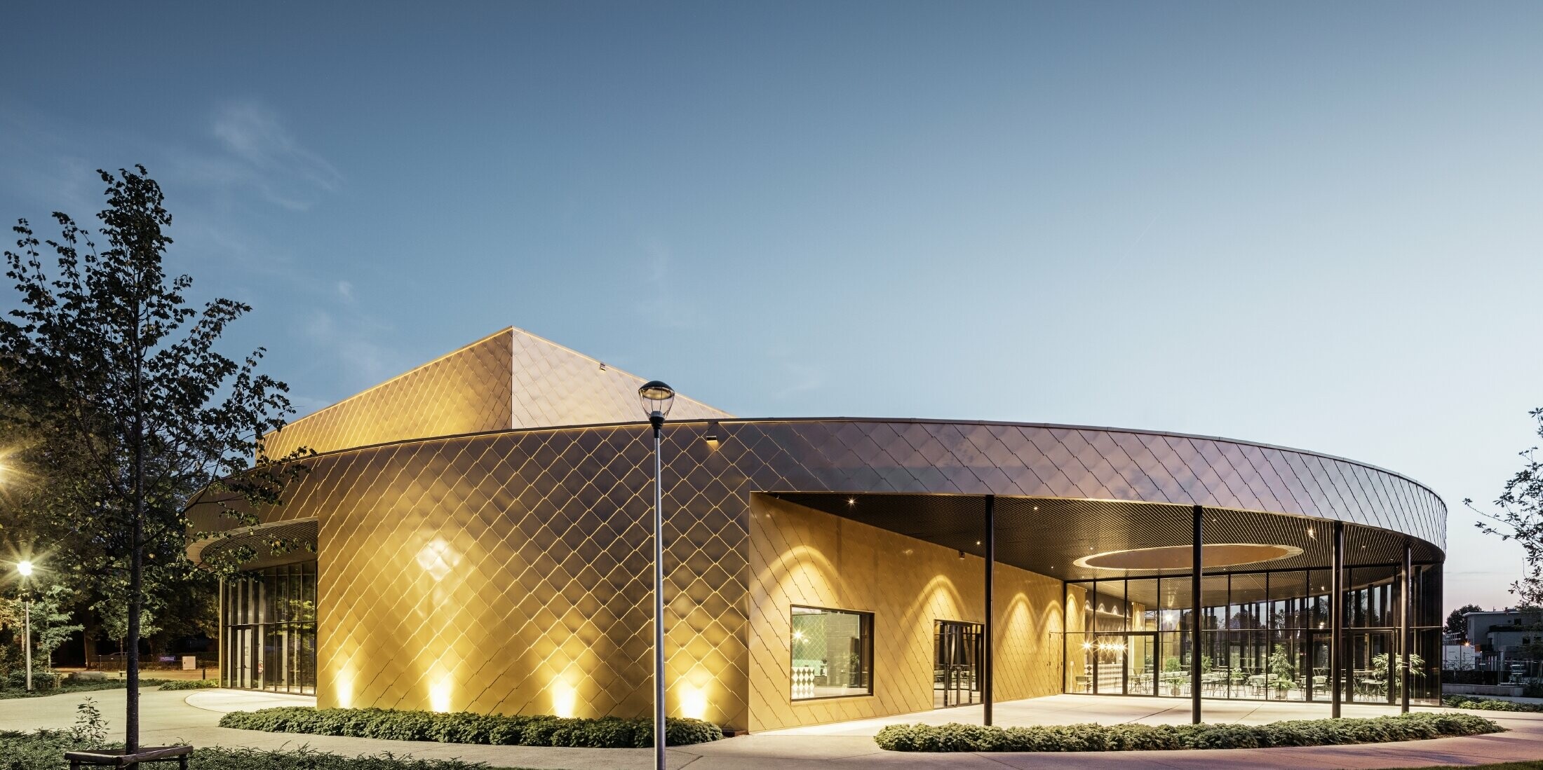 Image of the polyvalent chapels at dusk with PREFA’s rhomboid façade tile 44 × 44 in maya gold