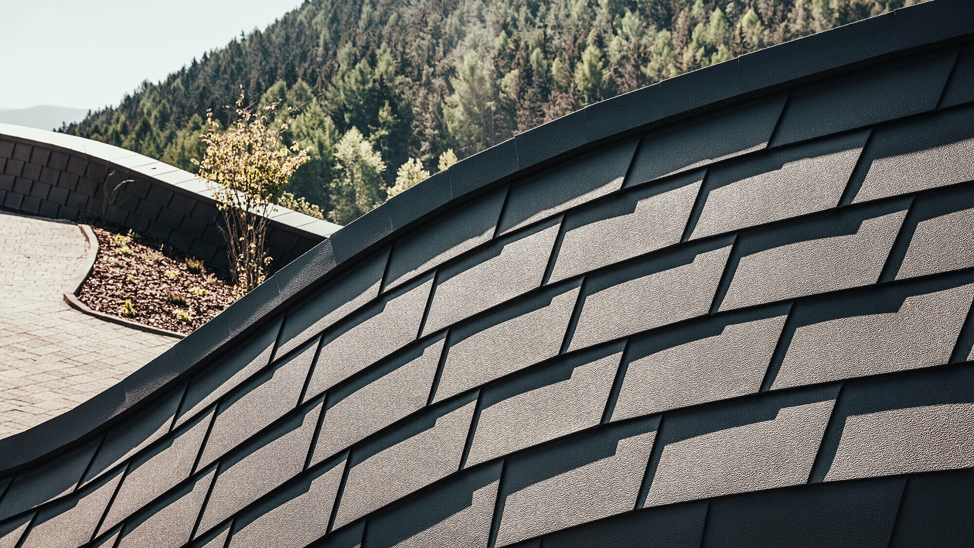 Detailed view of PREFA façade shingles in P.10 Brown. A section of the forest can be seen in the background