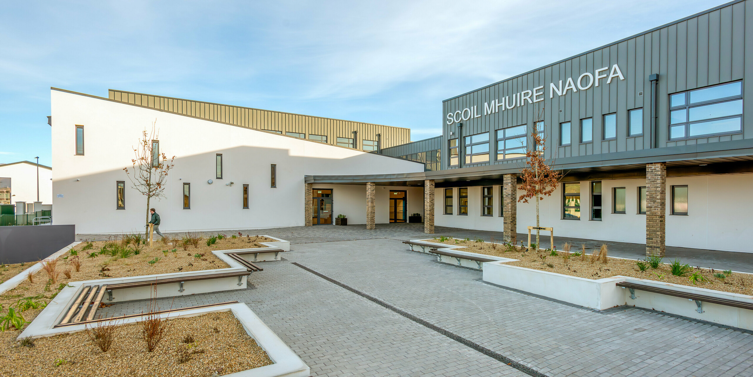 The inviting outdoor area of Scoil Mhuire Naofa in Carrigtwohill, Ireland, with seating and well-kept planting. The PREFALZ aluminium façade in P.10 light grey gives the school building a long-lasting and weather-resistant elegance, which is complemented by clean lines and functional design.