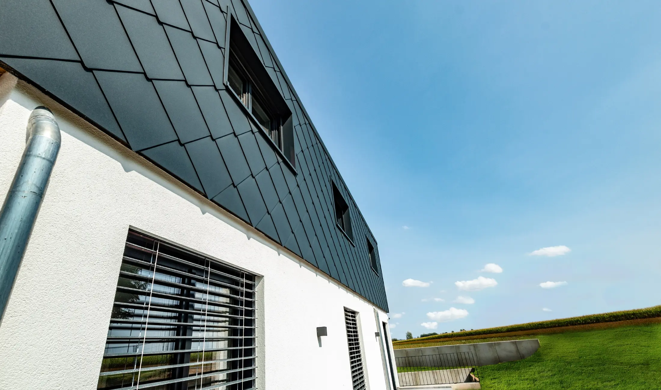 Large-format 44 cm PREFA rhomboid façade tile in anthracite in combination with a white rendered façade.