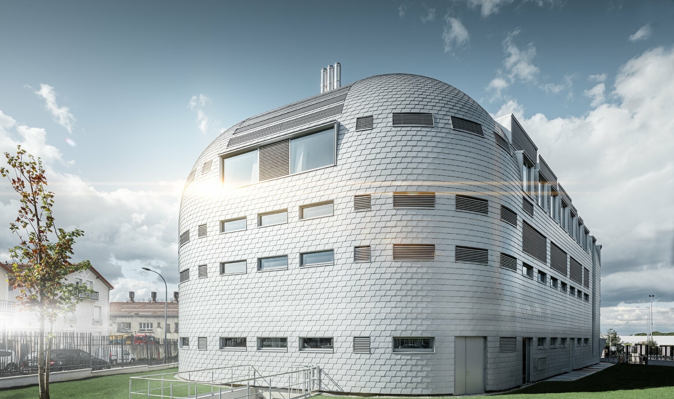 Modern office building covered with the bright PREFA aluminium shingles in metallic silver. The dome was clad in handmade roof shingles.