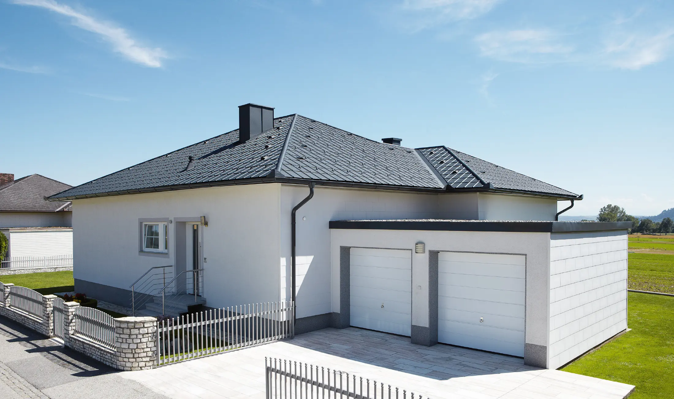 The newly built bungalow with a tent roof was covered with PREFA roof tiles in P.10 anthracite. A double garage was built to the right of it, photographed from the street.