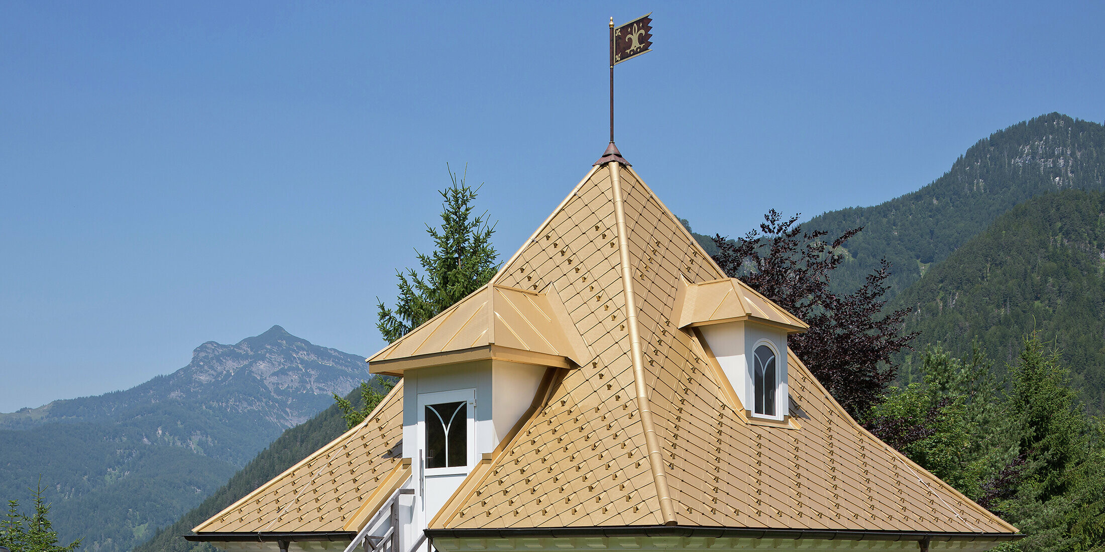 Detailansicht des Aluminiumdaches eines kleinen Anbaus. Das Goldene Dach liegt in Tirol, umgeben von einem gepflegten Garten und einer beeindruckenden Alpenkulisse.