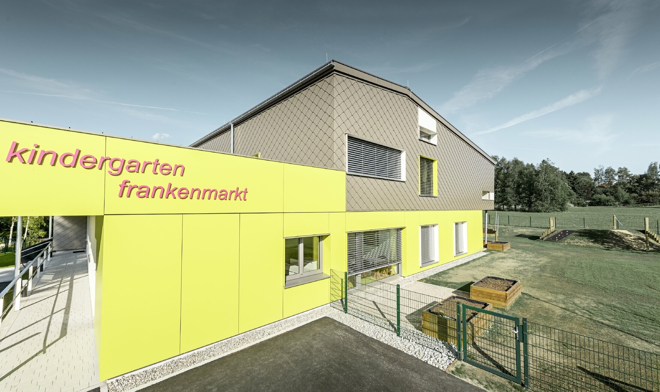 The façade of the kindergarten in Frankenmarkt was partially clad in the PREFA rhomboid façade tile in bronze. The rest of the façade was clad in façade tiles in yellow. The lettering for the kindergarten is also displayed.