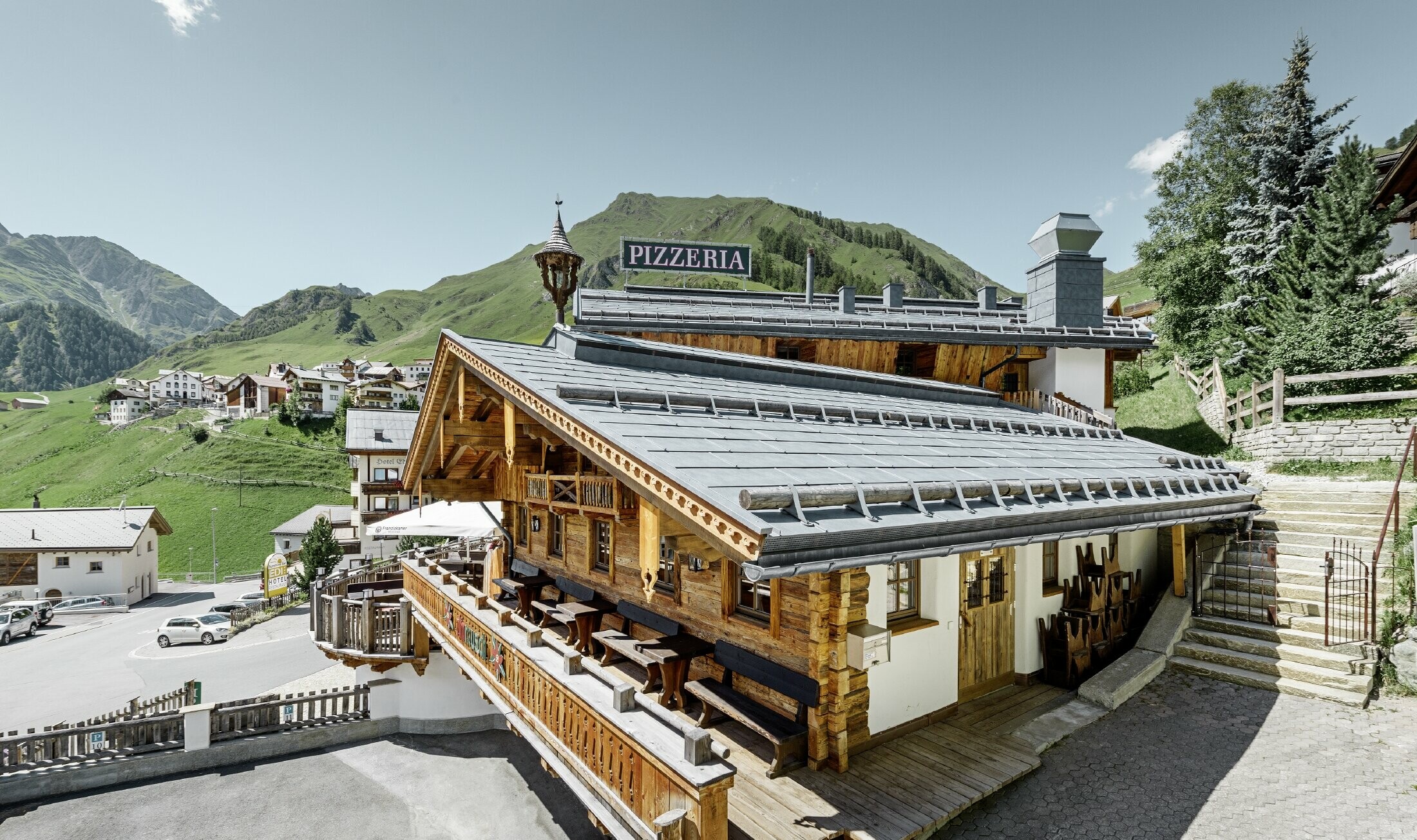 Restaurant Almrausch with a mountainous backdrop and a PREFA roof with FX.12 roof panels in stone grey and mountain snow guard brackets