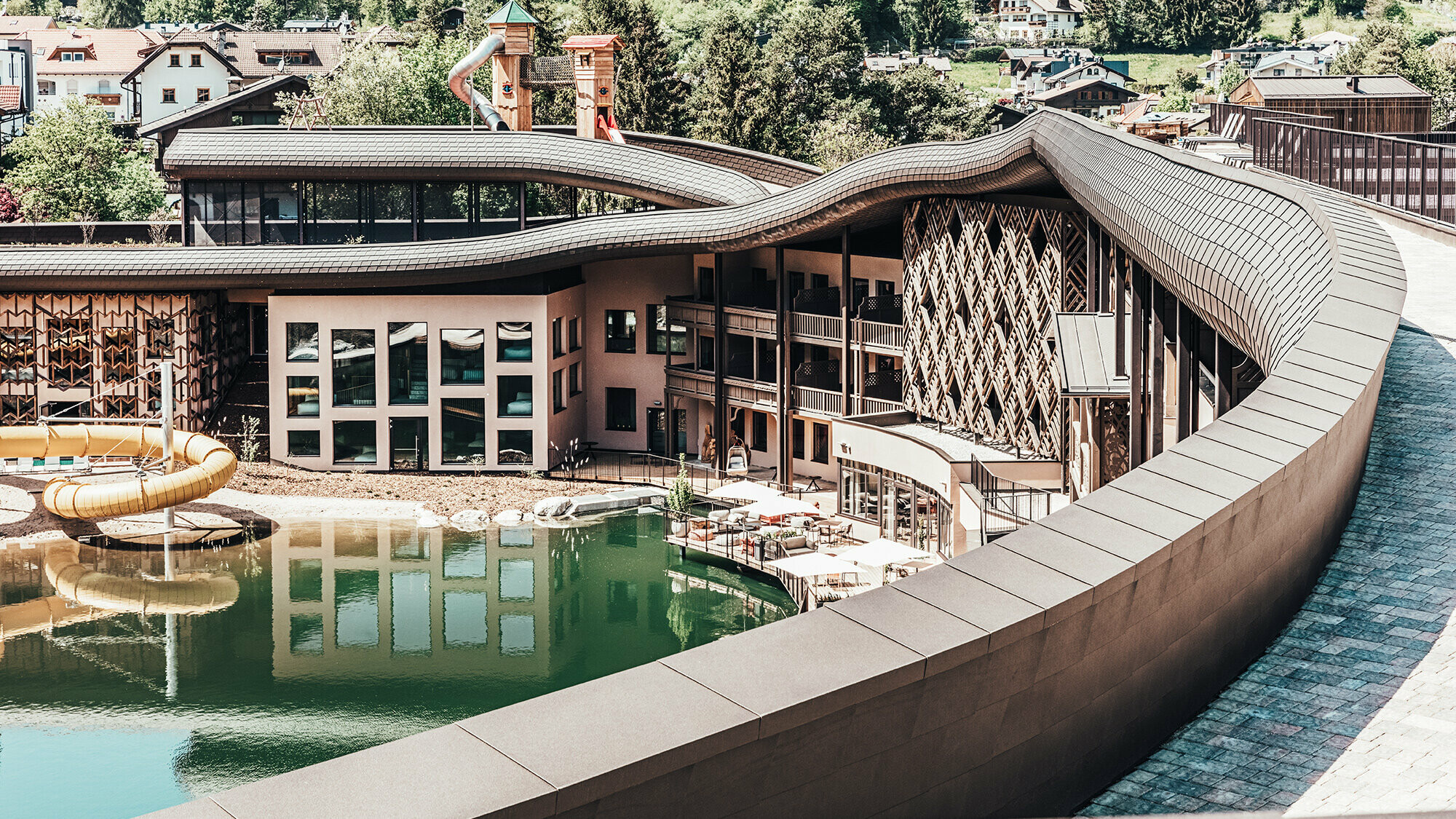 View of the hotel complex, the roof wave runs across the entire buildingm a lake can be seen in front of the hotel