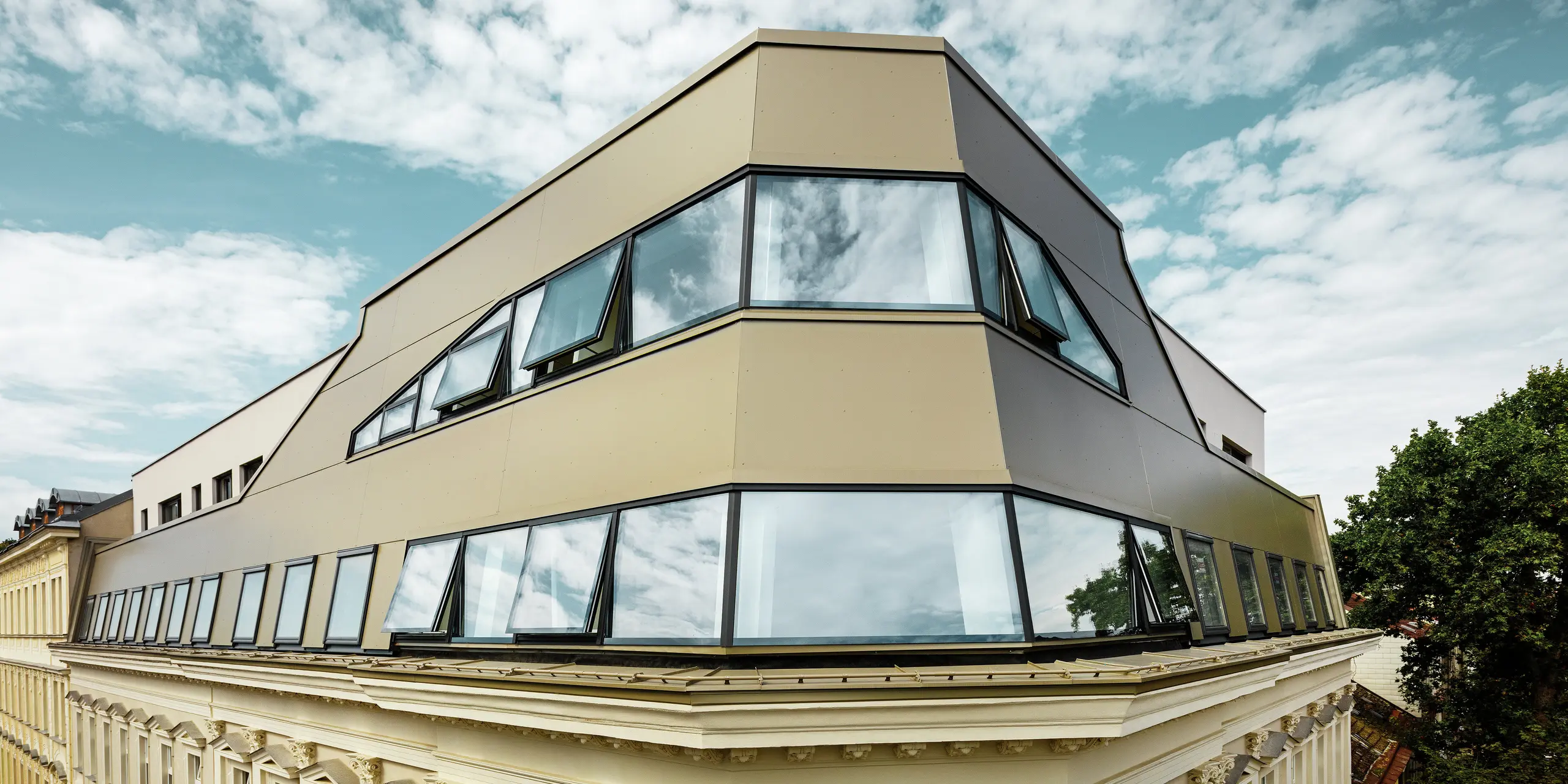 Die markante Dachkante des sanierten Gründerzeithauses in der Schloßhofer Straße in Wien zeigt den gelungenen Einsatz von PREFA Aluminium Verbundplatten in Bronze. Die Fassadengestaltung verbindet moderne Architektur mit dem klassischen Stil des Bestandsgebäudes.
