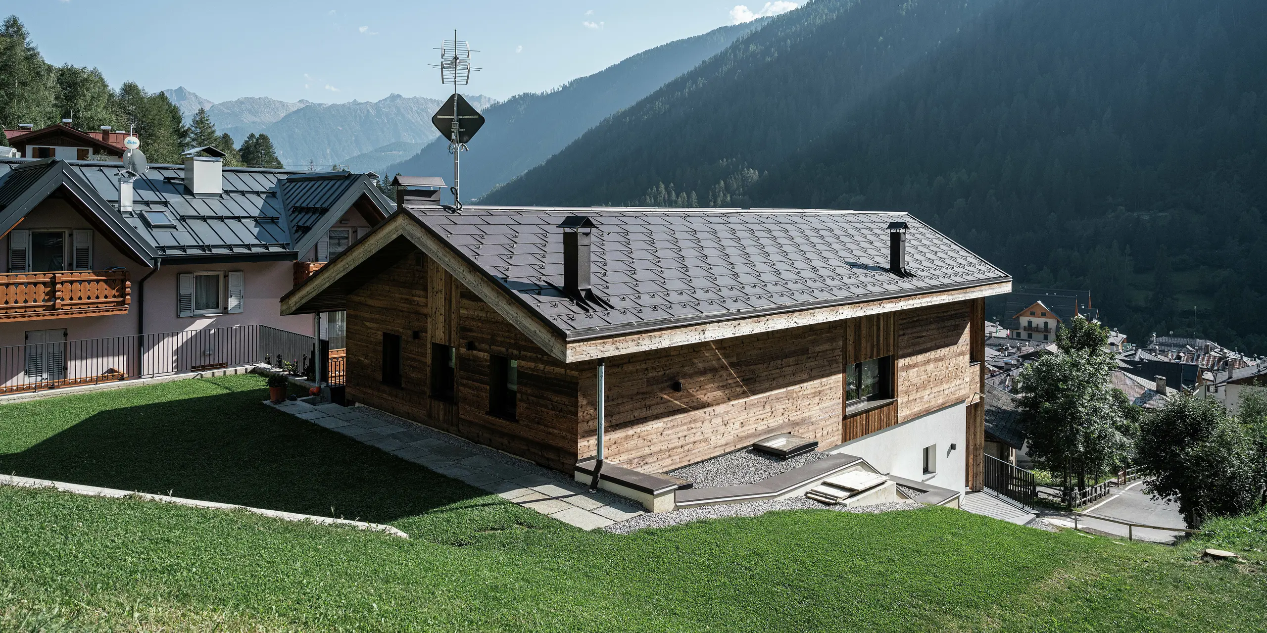 Rückseite eines modernen Berghauses in Cogolo, im italienischen Val di Sol, mit langlebigen PREFA Dachplatten R.16 in P.10 Braun. Das robuste Aluminiumdach fügt sich perfekt in die alpine Landschaft ein und schützt das Gebäude zuverlässig vor Schnee, Wind und Wetter. Klare Linien und höchste Belastbarkeit machen dieses Dach zur idealen Lösung für hochgelegene Regionen.