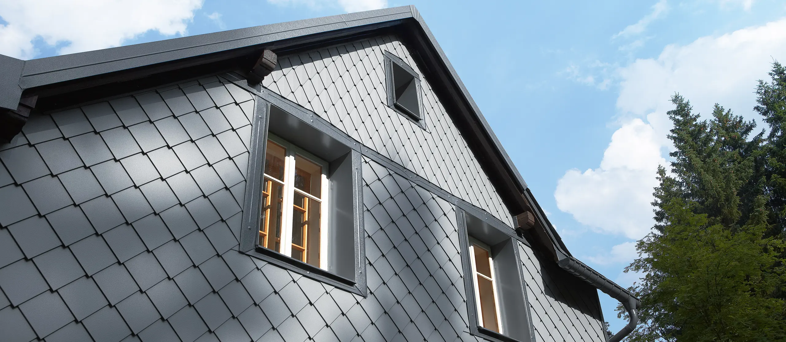 The side of a building that faces the direction of the prevailing weather clad with PREFA’s rhomboid façade tile 20 × 20 and small-format rhomboid tile on the façade