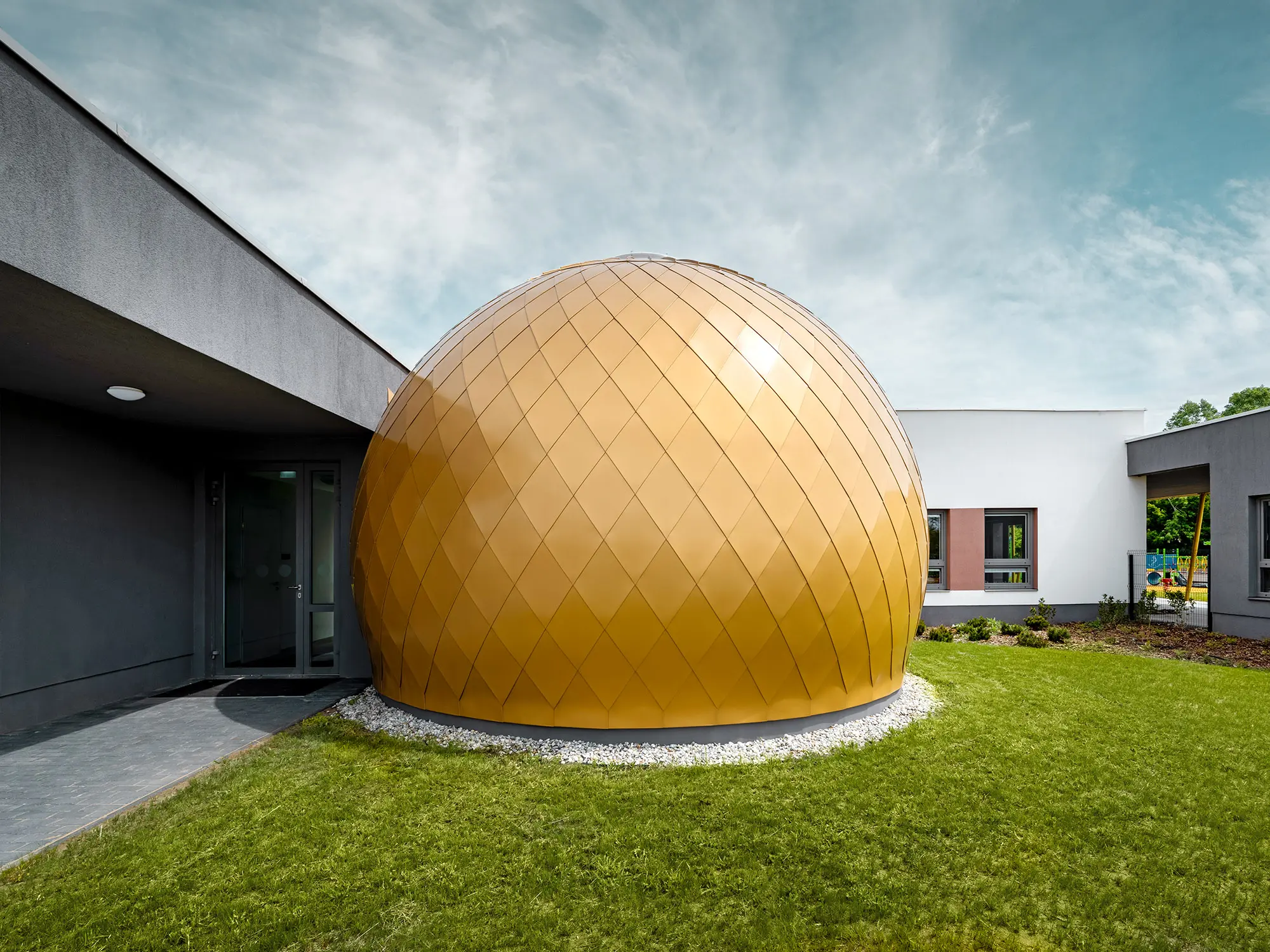 One of the three round rooms of the day nursery designed by László Erdei from the side, the plaster façade as well as the playground are partially visible next to it and behind it. 