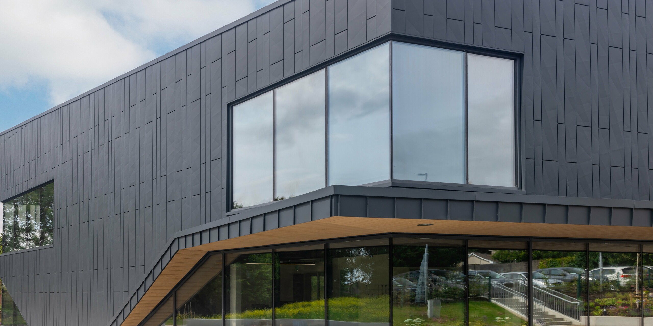Detailed view of the modern façade of the CREW building in Galway, Ireland, designed with PREFA Siding.X façade panels and PREFALZ in the colour P.10 anthracite. The striking corner window emphasises the clear lines and innovative architecture of the building. The anthracite-coloured aluminium cladding lends the building a timeless elegance and demonstrates the high quality of PREFA aluminium products.