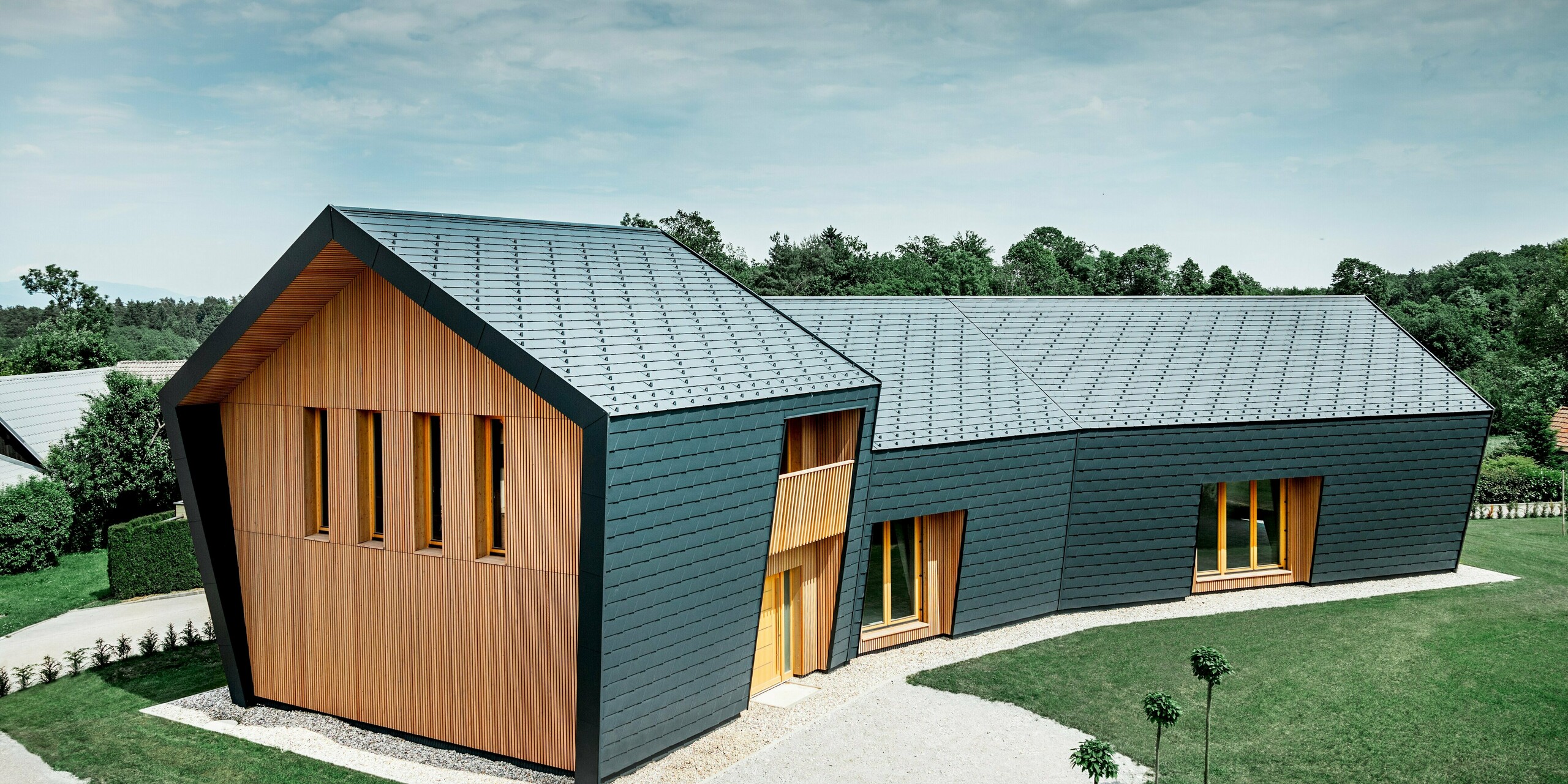 Gesamtansicht der Boulderhalle in Skofja; Die Kletterhalle ist am Dach und der seitlichen Fassade komplett mit der anthrazitfarbenen Schindel DS.19 von PREFA verkleidet. An der Stirnseite ist die Fassade mit hellem Lärchenholz verschalt.