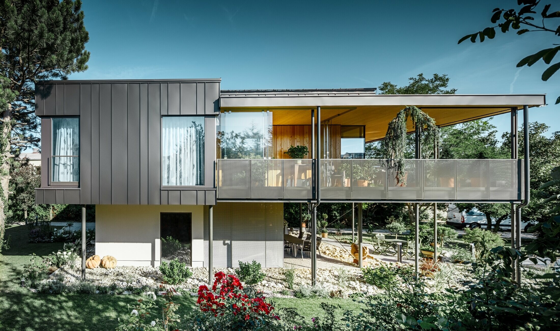 Modern detached house, resembling a tree house, surrounded by an ample garden full of trees, with a modest PREFA single-lock standing seam façade in black grey