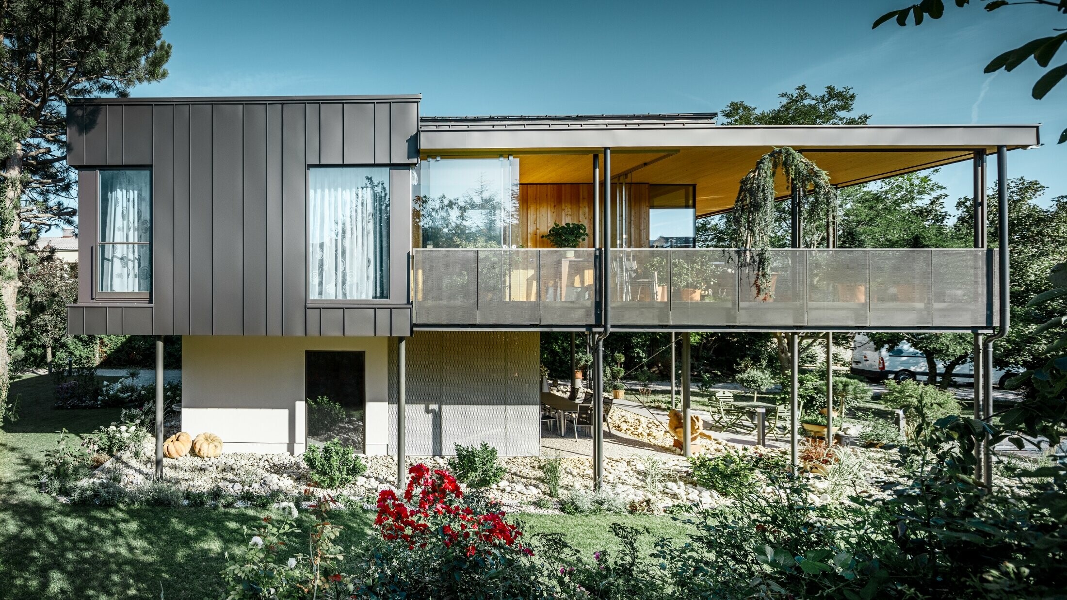 Modern detached house, resembling a tree house, surrounded by an ample garden full of trees, with a modest PREFA single-lock standing seam façade in black grey