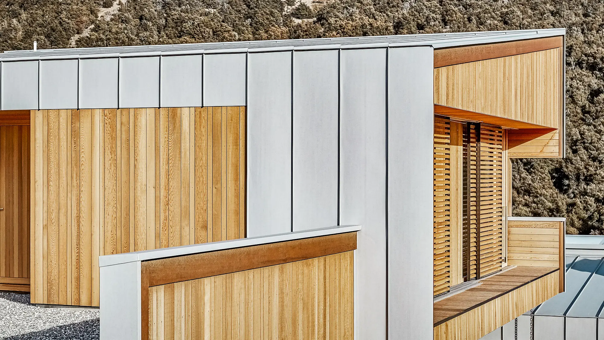 A shot of the building's evenly matt Prefalz envelope and timber elements, the bush forest partially visible behind it.