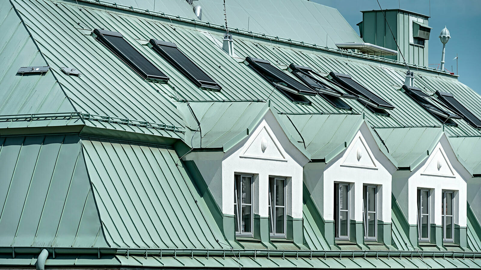 Close-up view of the Prefalz roof in P.10 patina green. Some windows of the building can be seen.