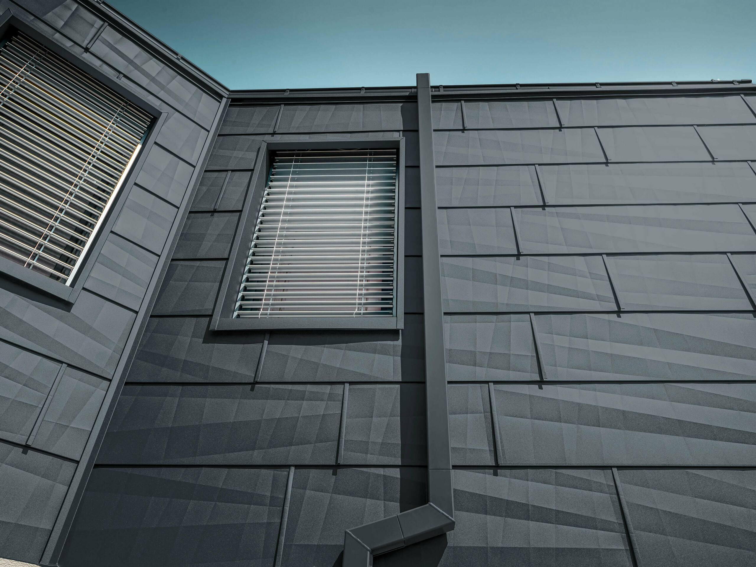 Façade clad with the PREFA FX.12 façade panel in anthracite, aluminium panels on the façade with the square downpipe, the square downpipe from PREFA in anthracite.