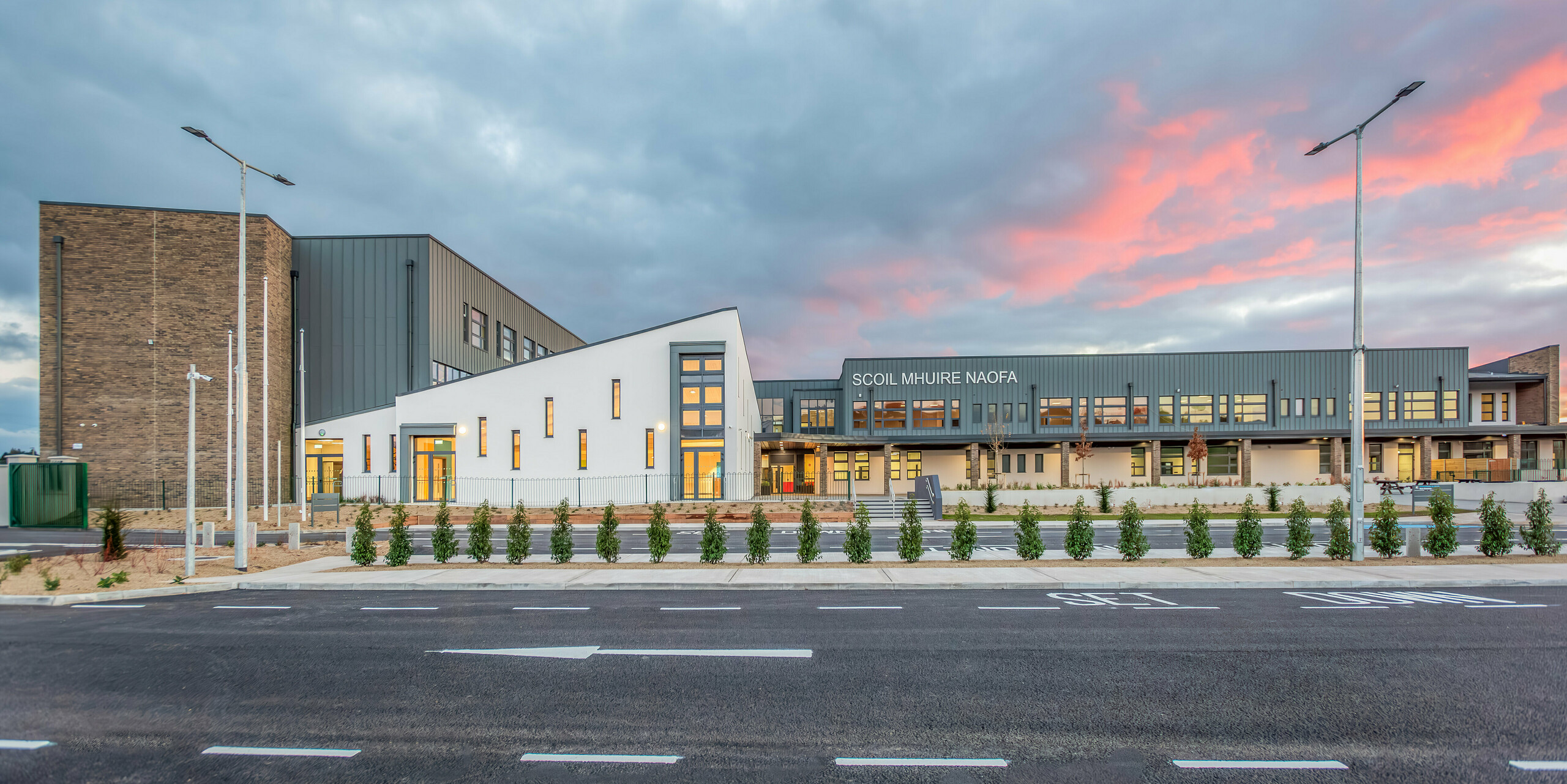 Front view of the new Scoil Mhuire Naofa in Carrigtwohill, Republic of Ireland, at sunset. The light grey PREFALZ aluminium facade combined with modern brick details and clean lines creates a harmonious and enduring architecture. The spacious outdoor area underlines the inviting atmosphere of the school.