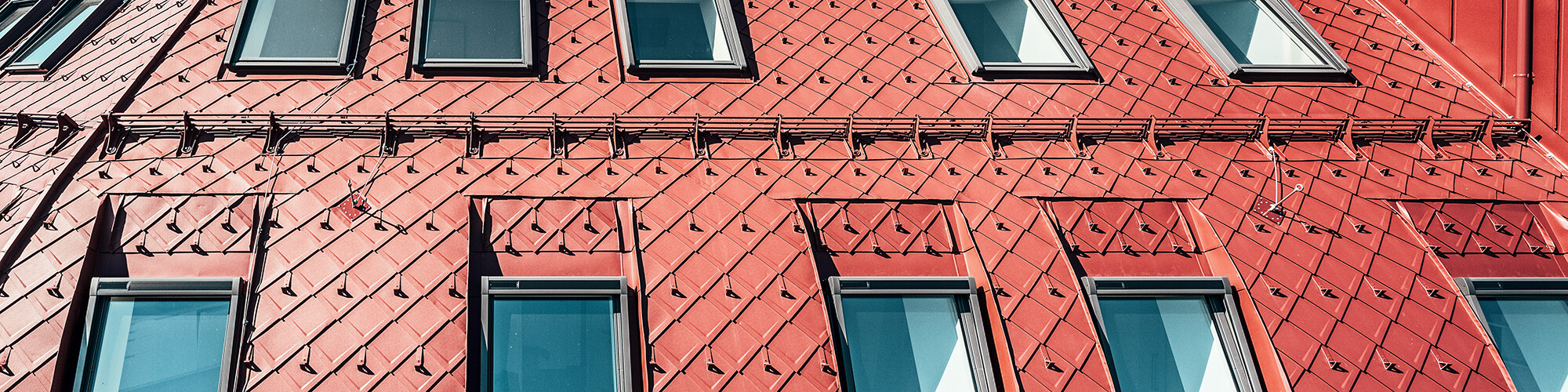 Close-up of the striking roofscape made of oxide red aluminium rhomboid tiles.