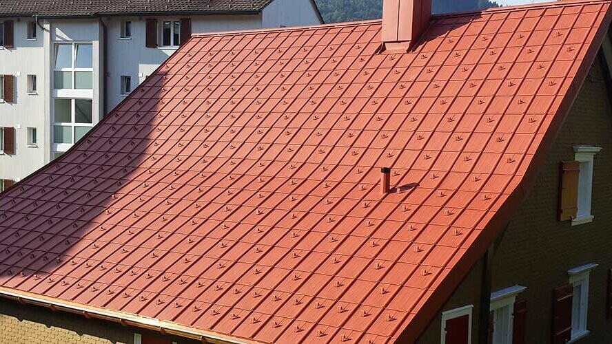 Gable roof covered with PREFA aluminium roof tiles. Brick-red roof with snow guards and chimney