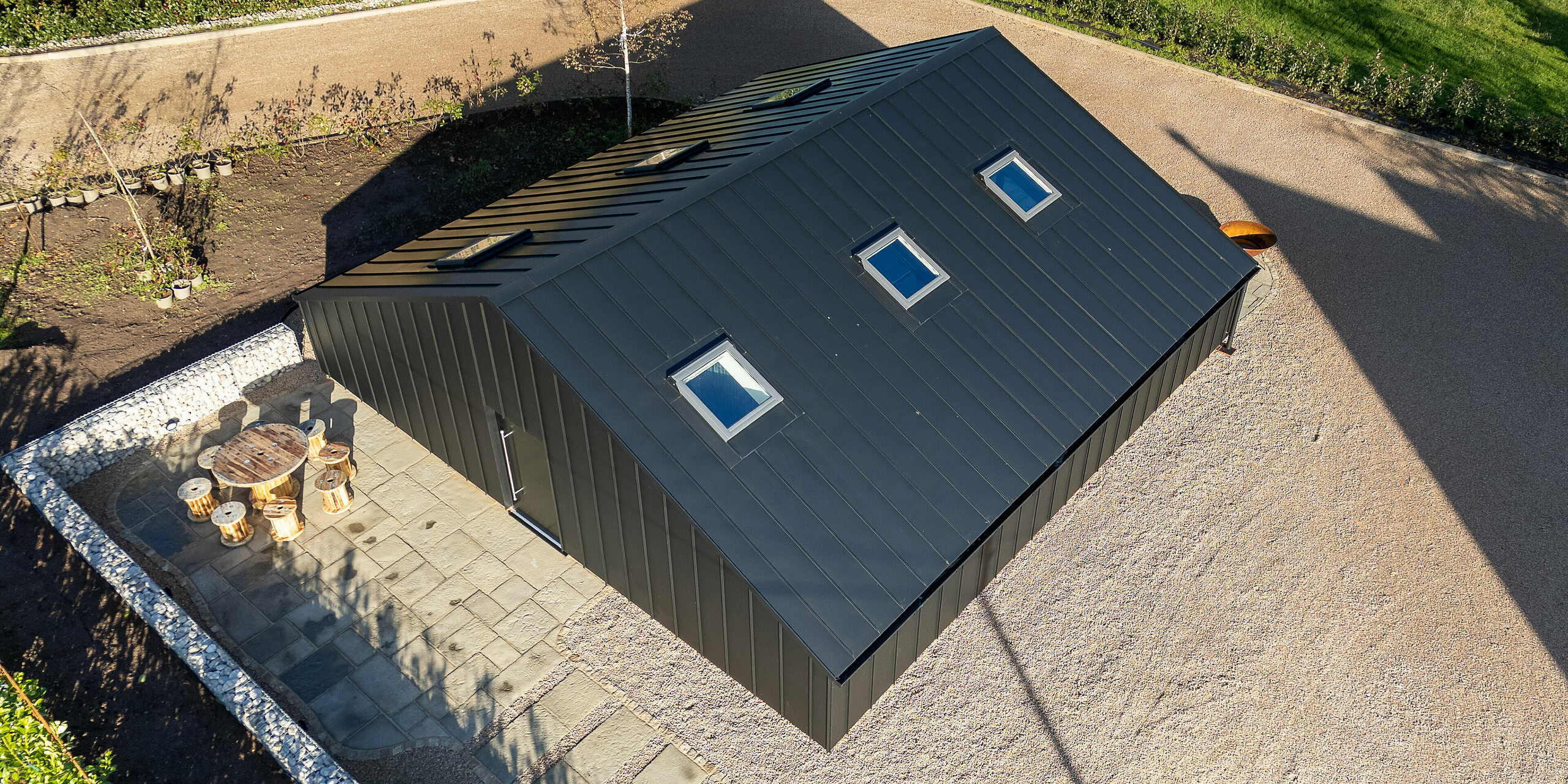 Aerial view of the modern leisure building in Ranton clad entirely with PREFA aluminum in P.10 black. The seamless PREFALZ standing seam roof with integrated roof windows emphasizes the clean, contemporary design. The durable, weather‑resistant aluminum shell provides long‑lasting protection while creating a striking architectural statement within the spacious outdoor setting.